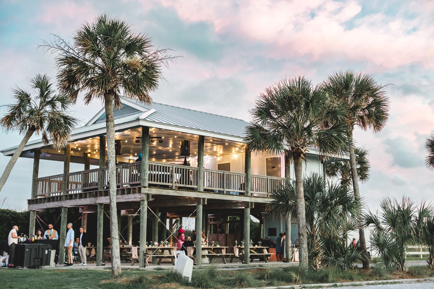 Coastal wedding venue with string lights and palm trees at sunset.