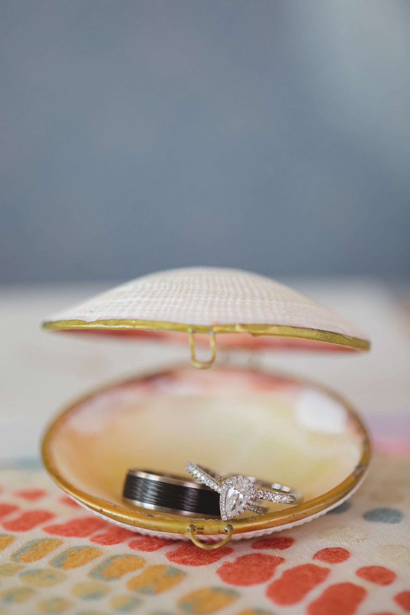 Wedding rings displayed inside an open decorative seashell on colorful patterned surface.