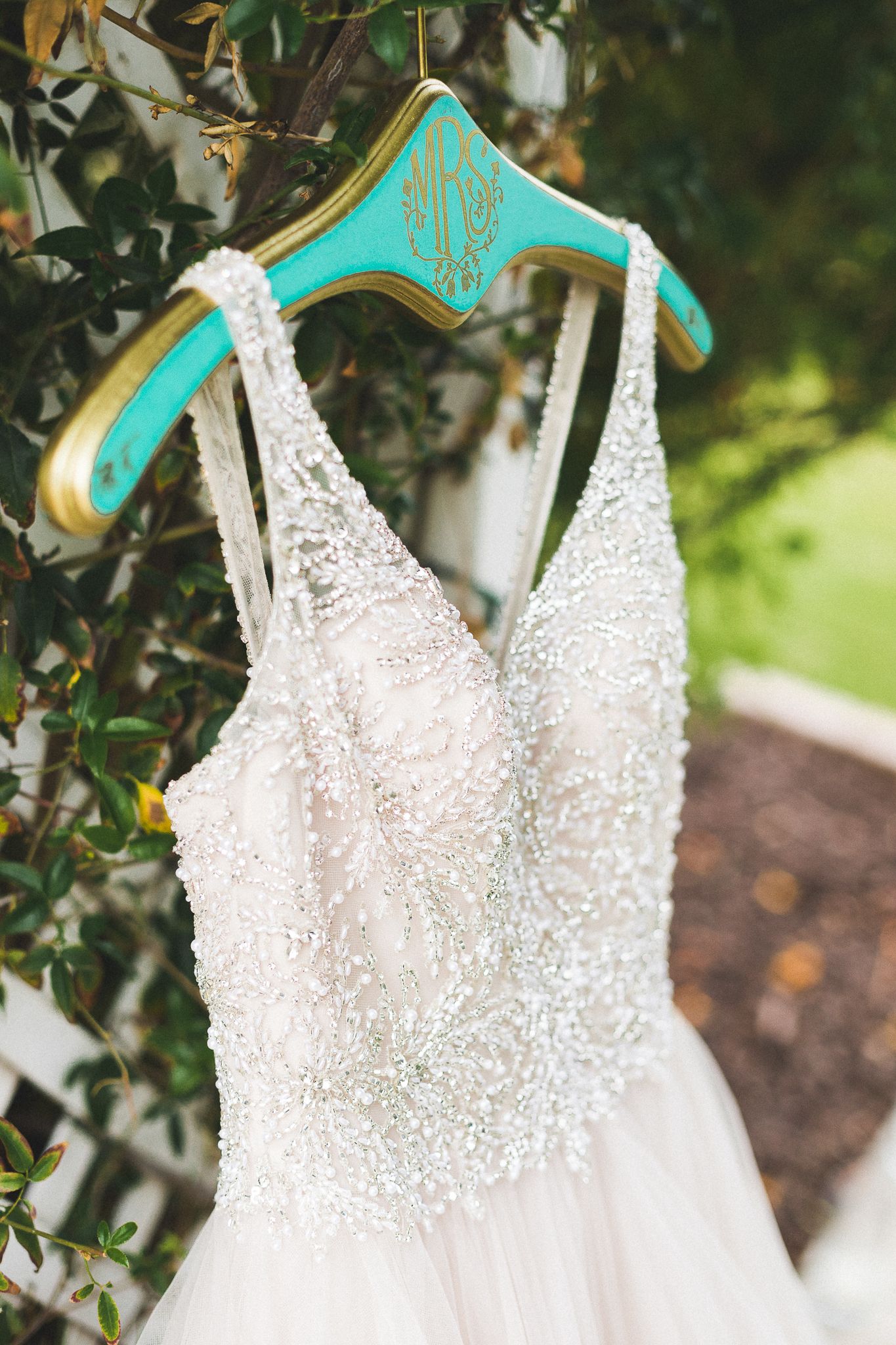 Beaded bridal gown with crystal embellishments hanging on a monogrammed teal and gold hanger.