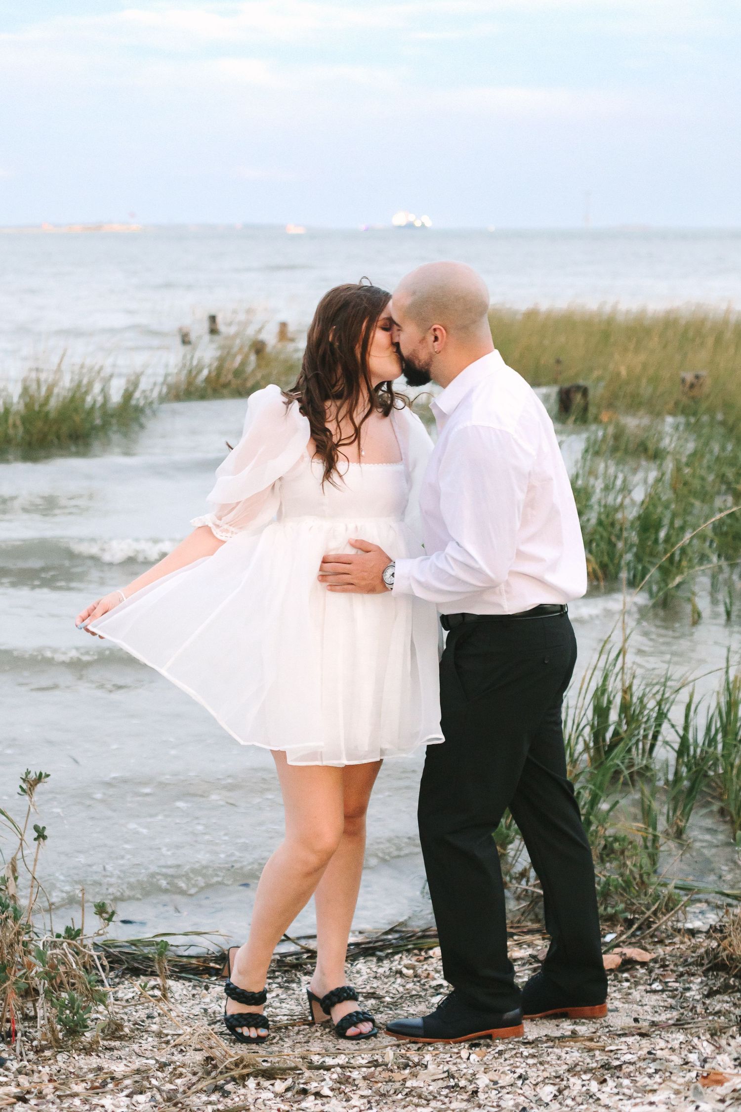 Couple nearly kissing on a rocky shoreline, woman in white dress, man in white shirt.