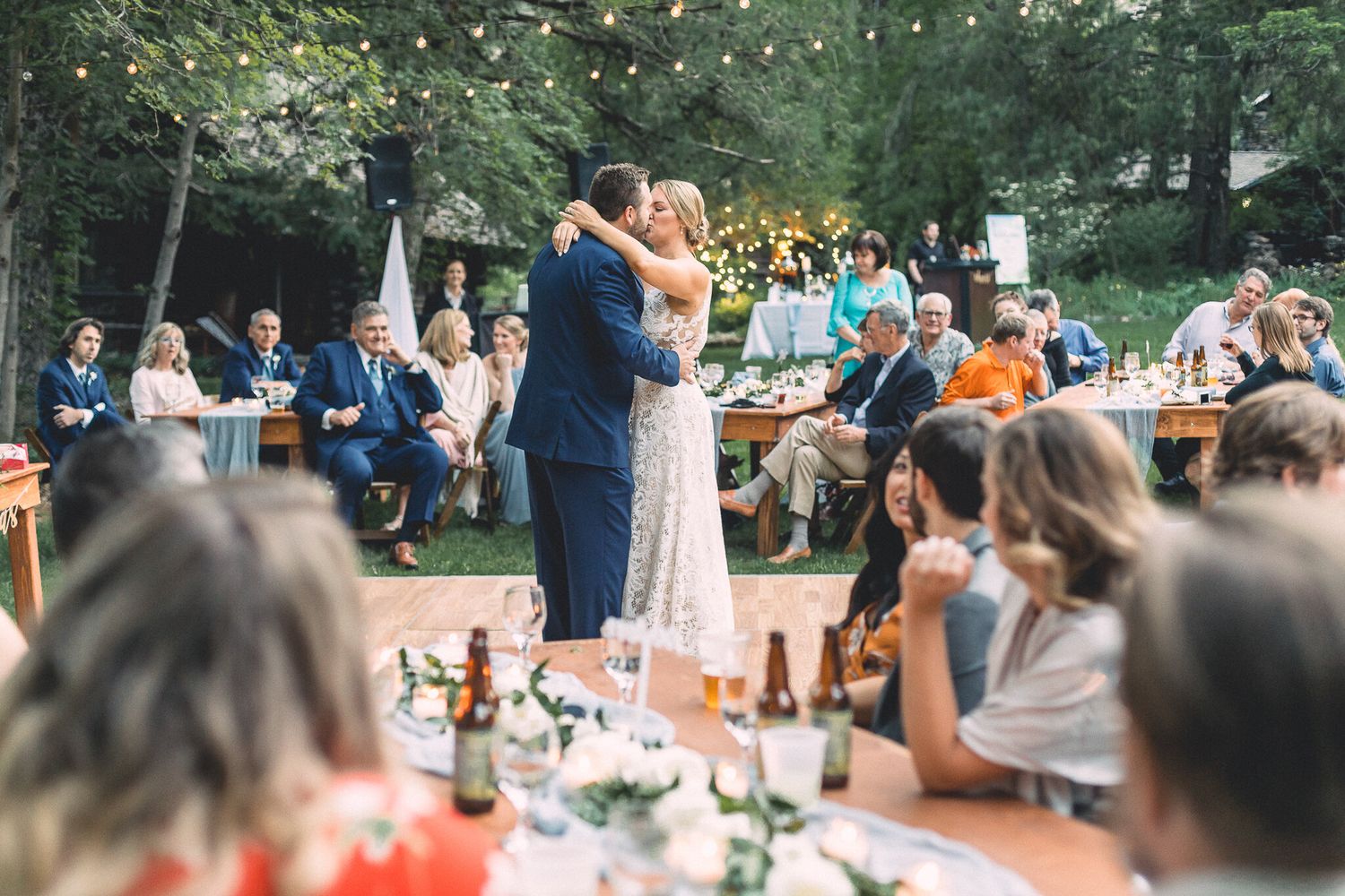 Couple sharing first dance at romantic outdoor wedding reception under string lights.