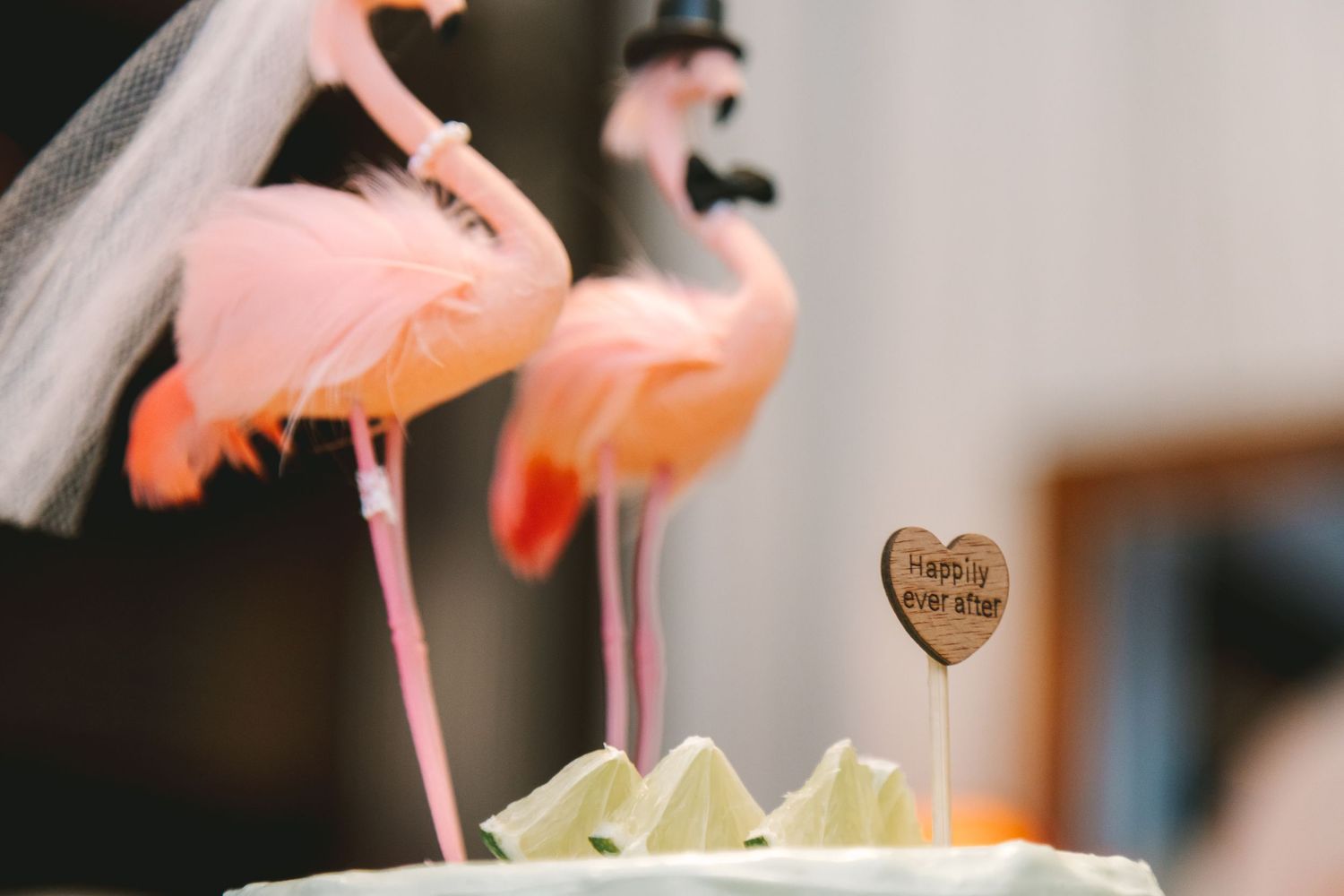 Pink flamingo wedding cake toppers with bride veil and groom hat with happily ever after sign.