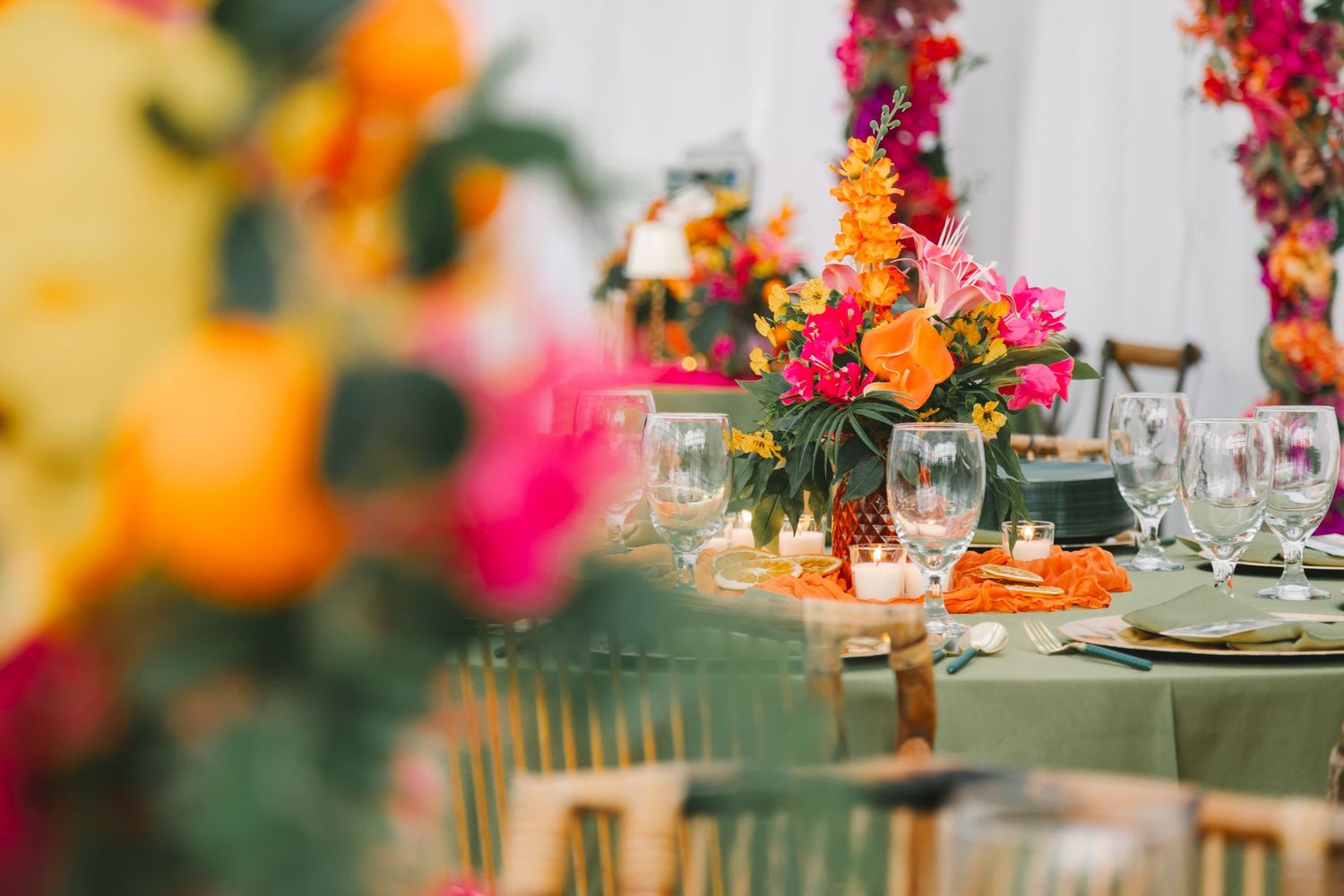 Tropical wedding reception tables with green linens, vibrant orange and pink floral centerpieces.