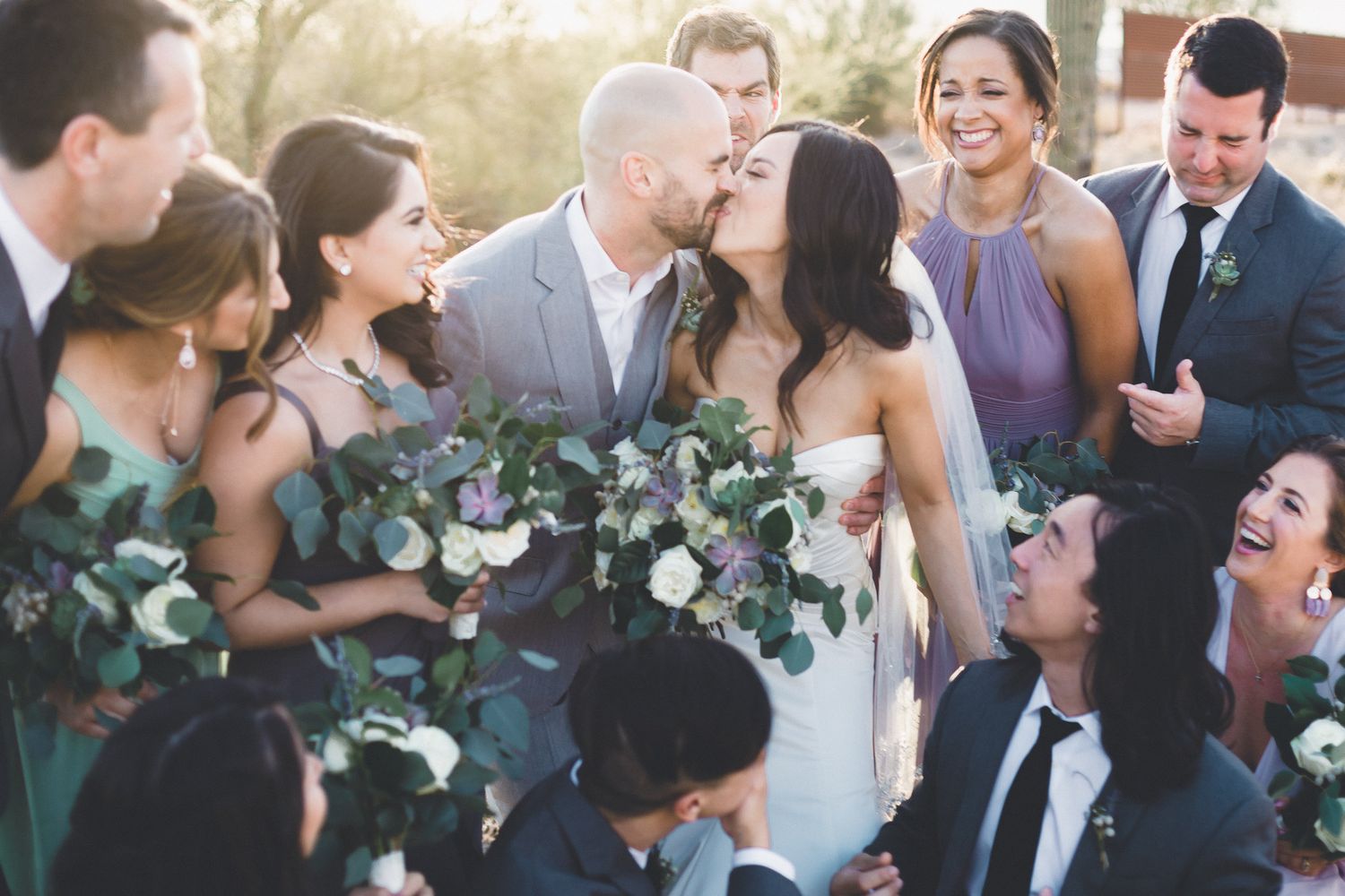 Joyful wedding party celebrating with bride and groom kiss surrounded by eucalyptus bouquets.