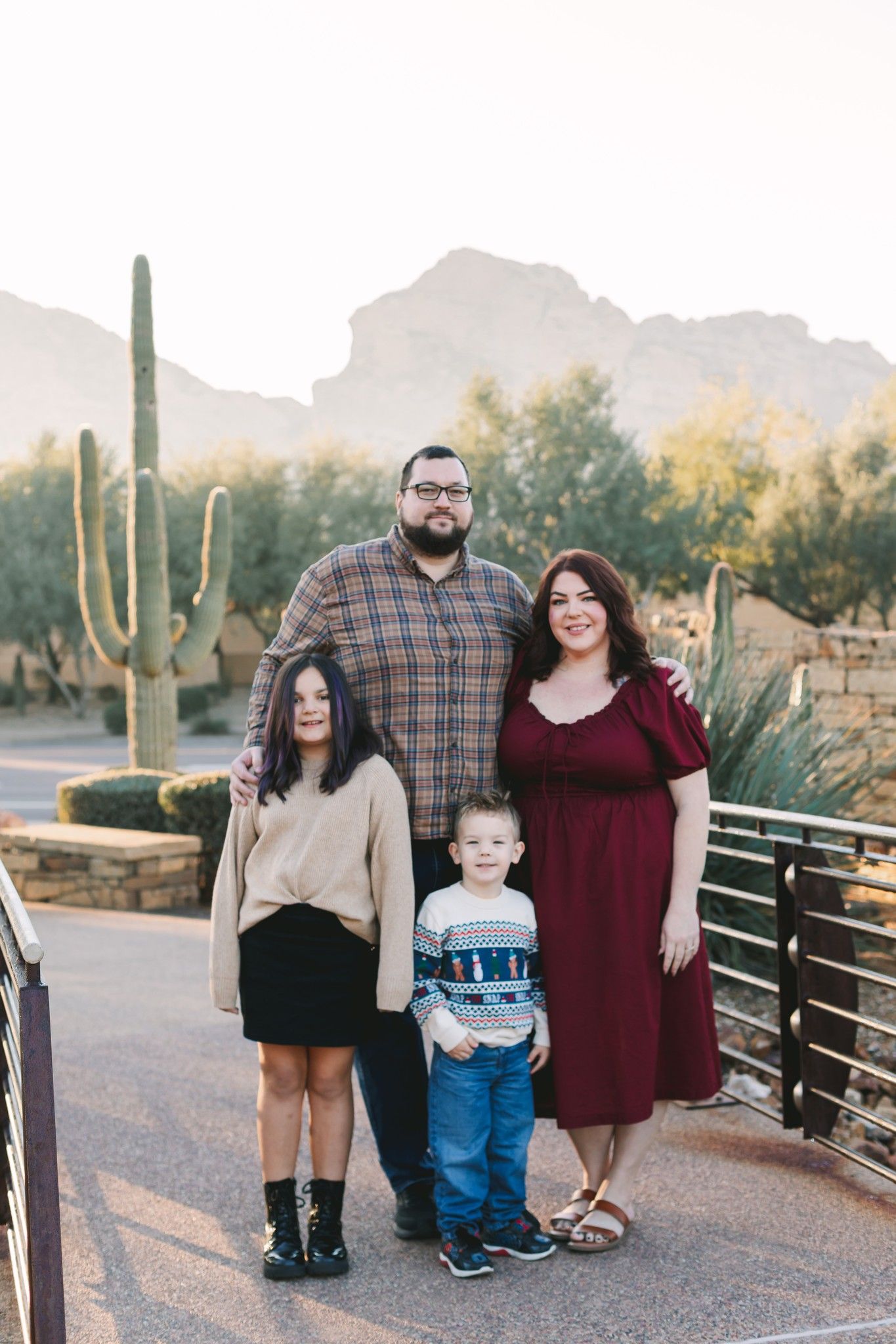 Family of four posing outdoors with saguaro cacti and mountain landscape in Arizona.
