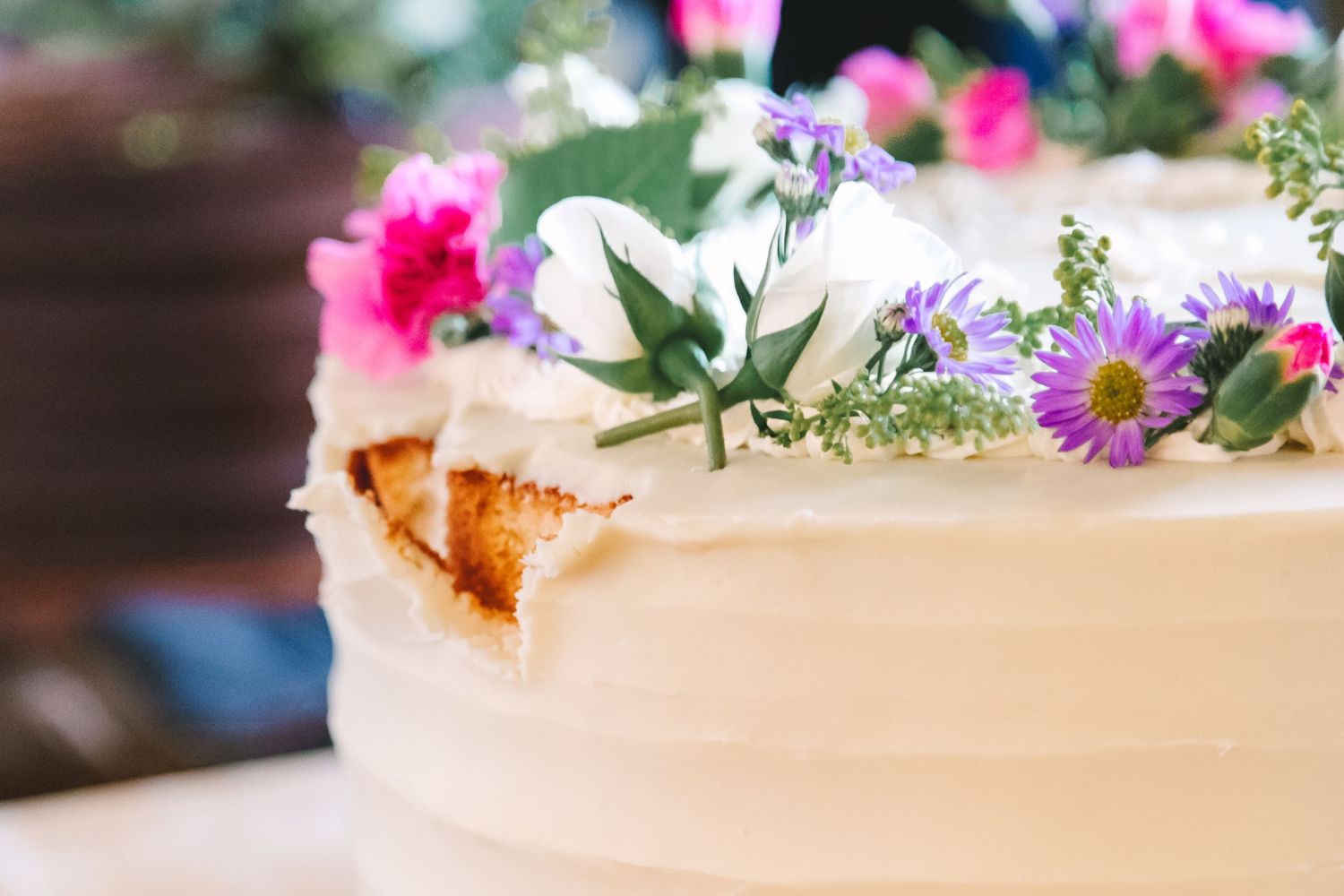 White wedding cake topped with fresh pink, purple, and white flowers with green foliage on display.