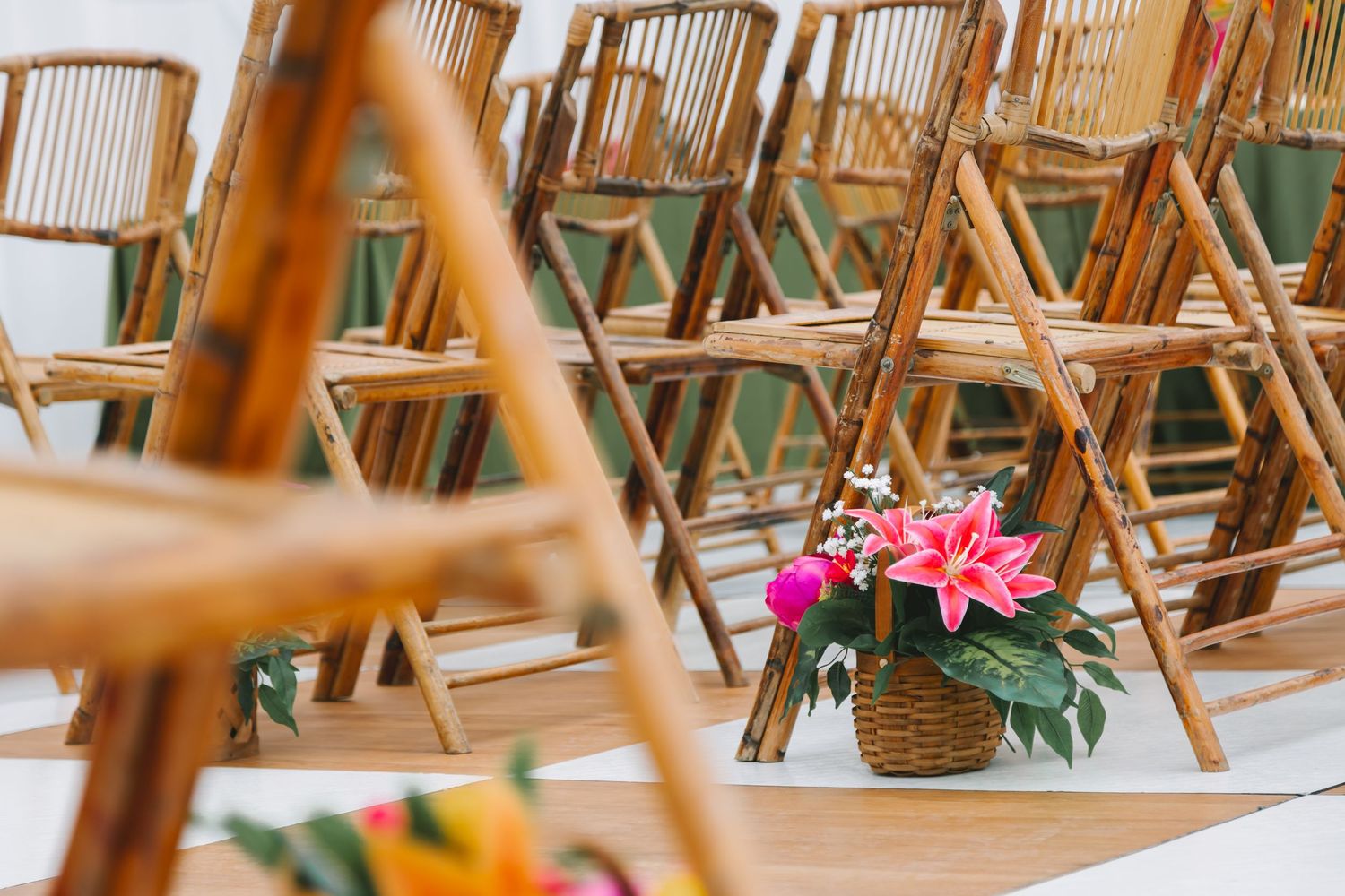 Wooden folding chairs arranged in rows with a wicker basket of pink lilies on a white aisle runner.