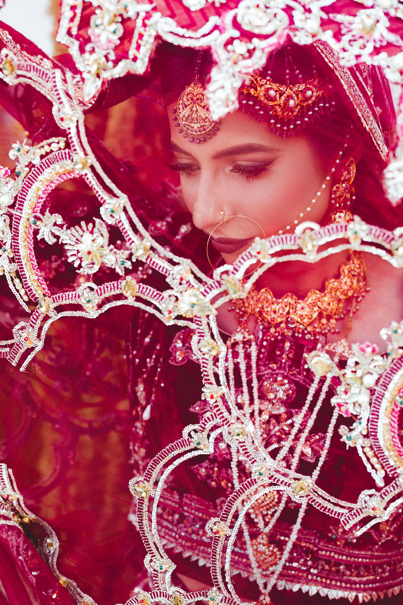 Close-up portrait of South Asian bride in ornate red bridal lehenga with intricate gold embroidery.