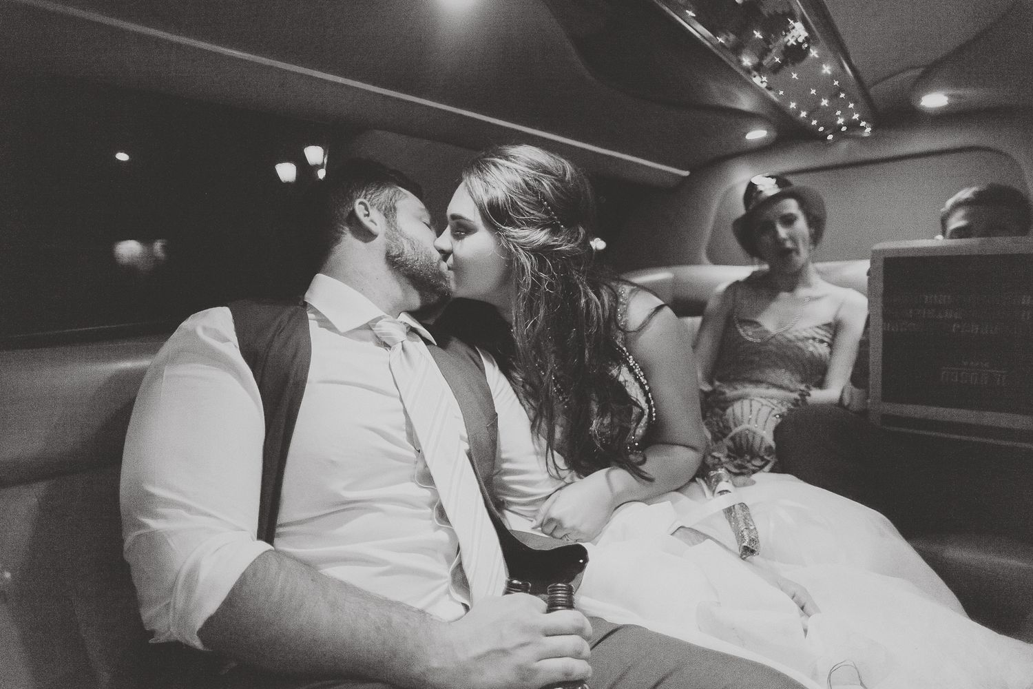 Black and white photo of a bride and groom kissing in a limousine on their wedding day.