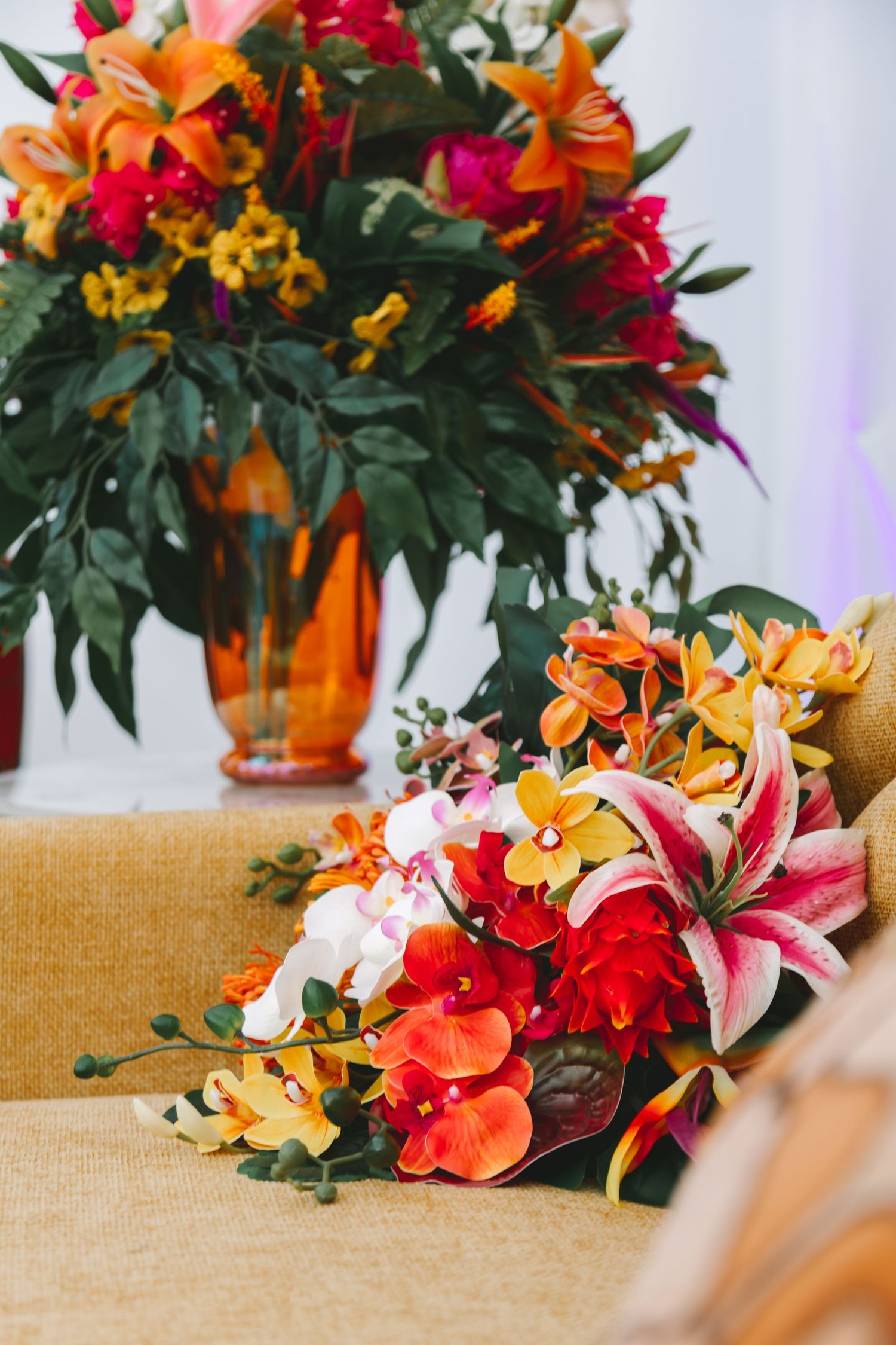 Vibrant orange, pink, and yellow wedding bouquet with lilies and orchids on burlap table runner.