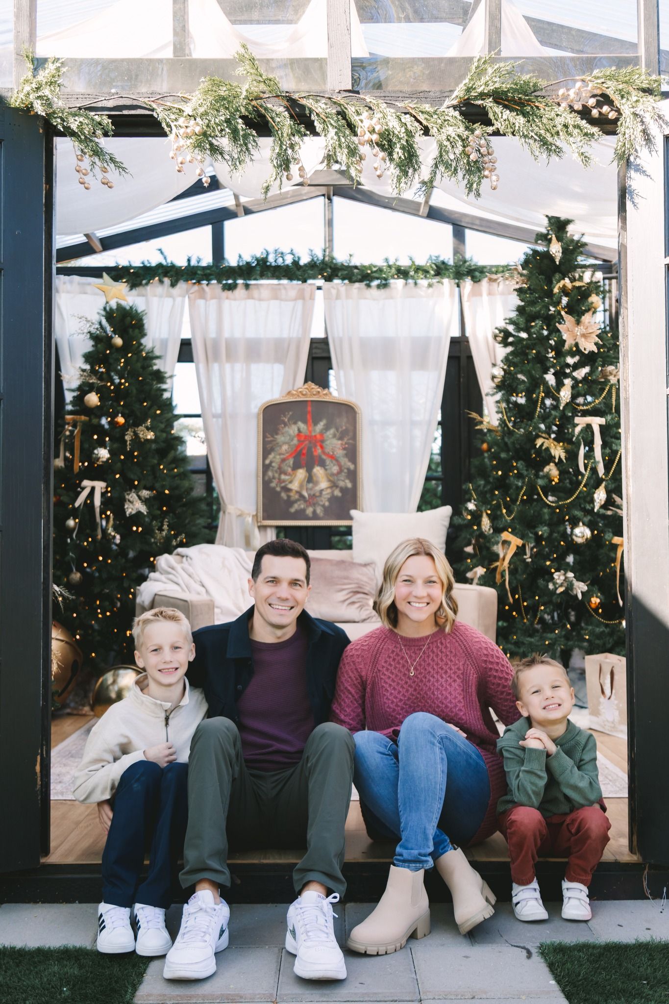 Family of four smiling together in a festive Christmas setting surrounded by decorated trees.