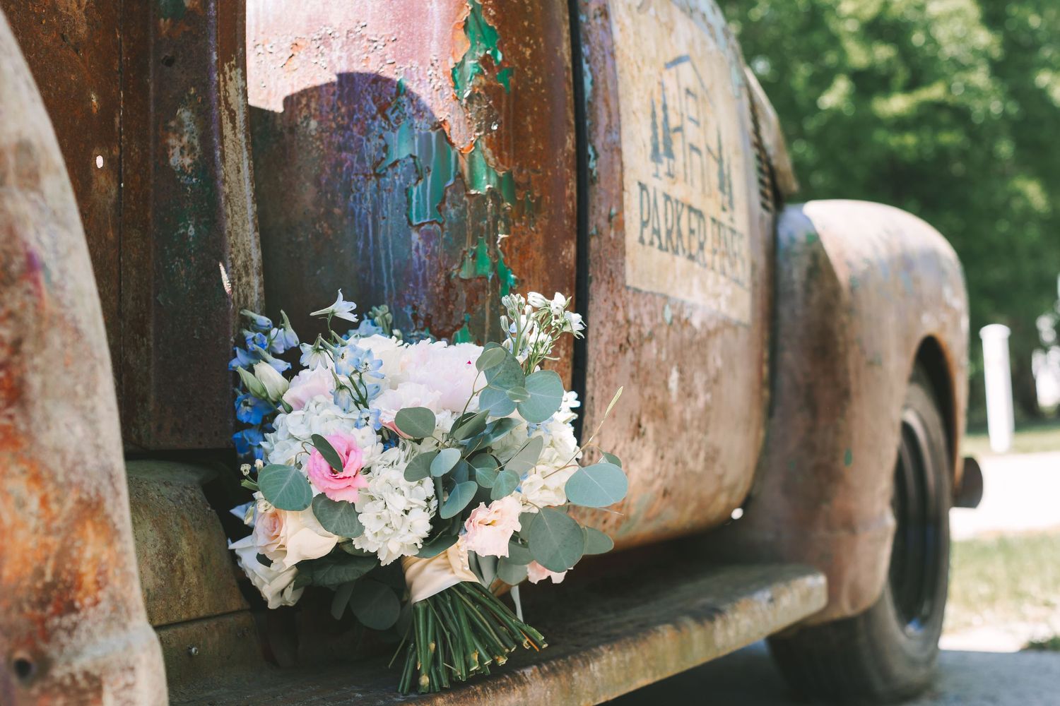 Rustic white and blue wedding bouquet with eucalyptus resting on the door of a vintage weathered truck.