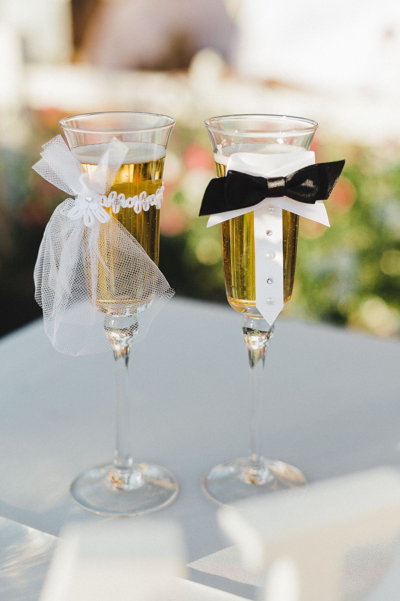 Two champagne flutes decorated as bride and groom with white veil and black bow tie.