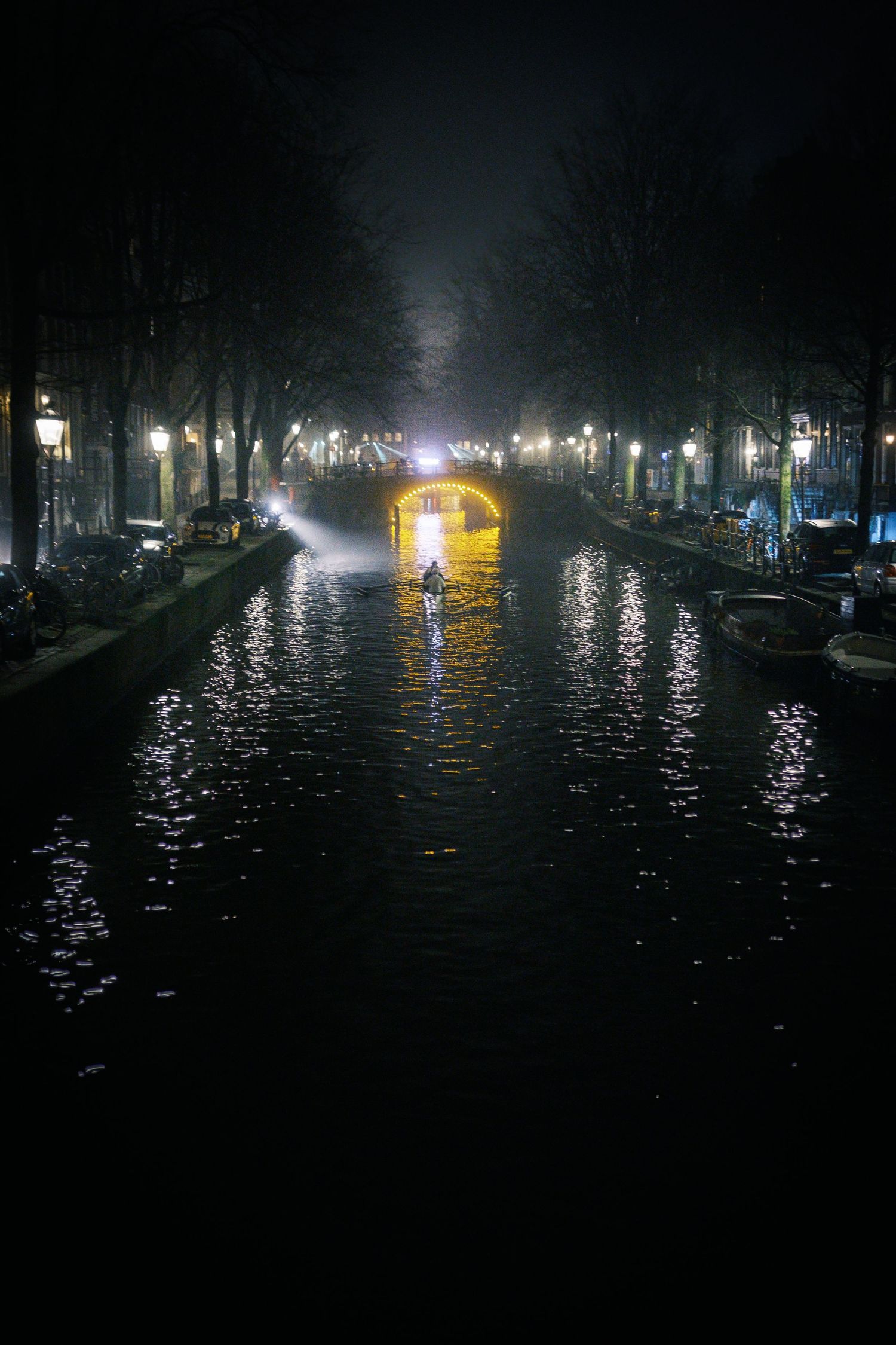 Night street photography in Amsterdam showing the city in heavy mist with soft lights, reflections and a cinematic urban atmosphere.