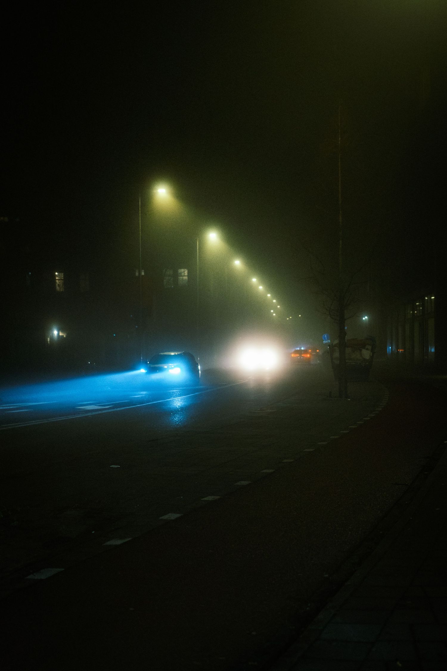 Night street photography in Amsterdam showing the city in heavy mist with soft lights, reflections and a cinematic urban atmosphere.