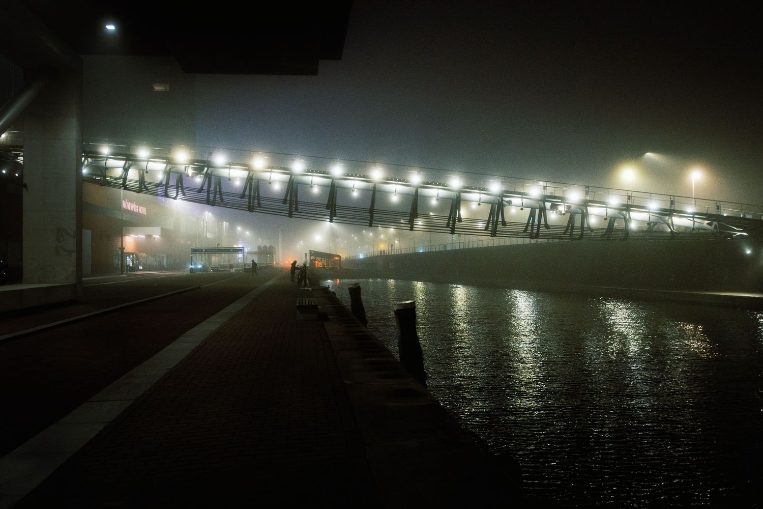 Night street photography in Amsterdam showing the city in heavy mist with soft lights, reflections and a cinematic urban atmosphere.
