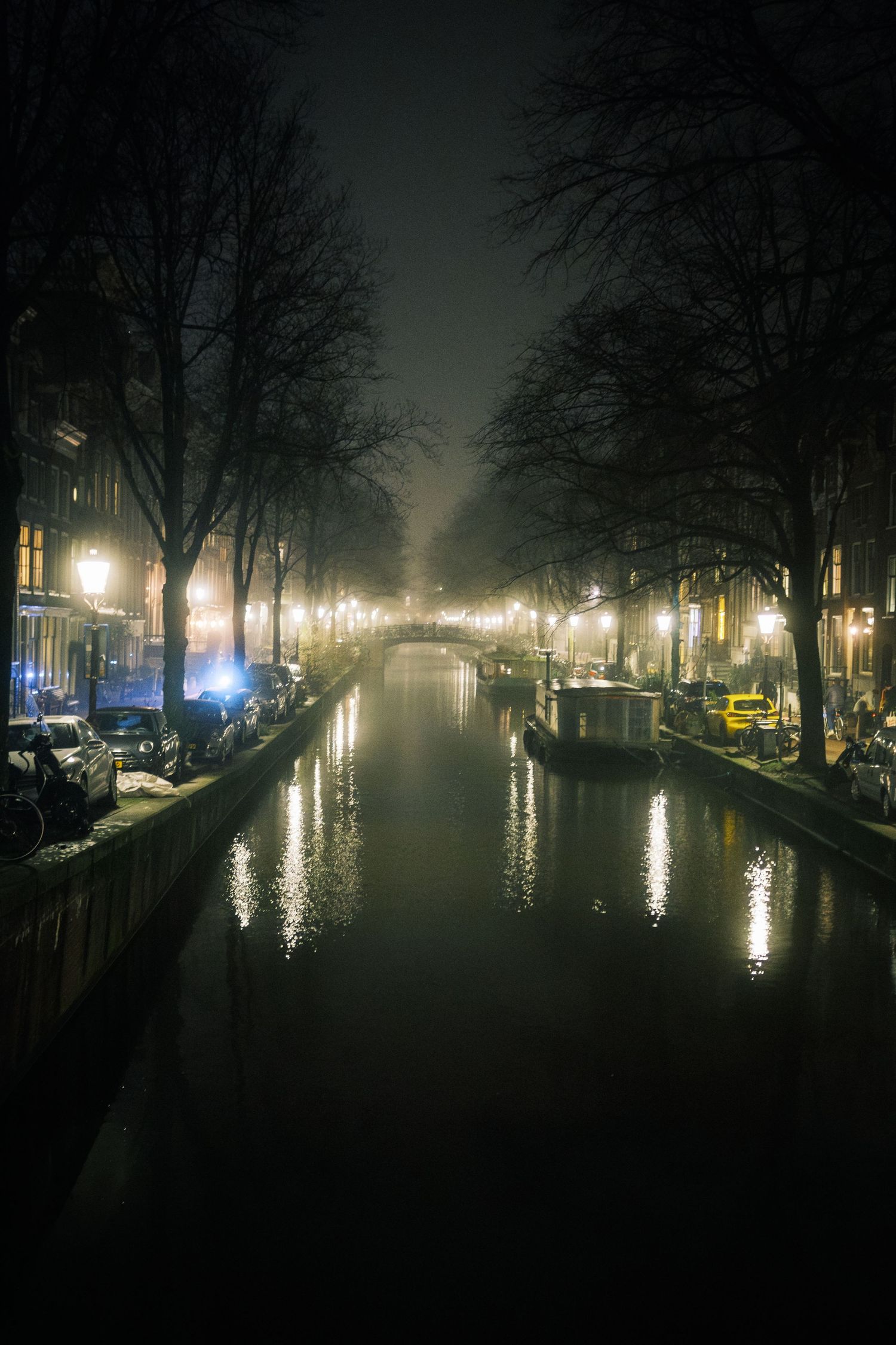 Night street photography in Amsterdam showing the city in heavy mist with soft lights, reflections and a cinematic urban atmosphere.