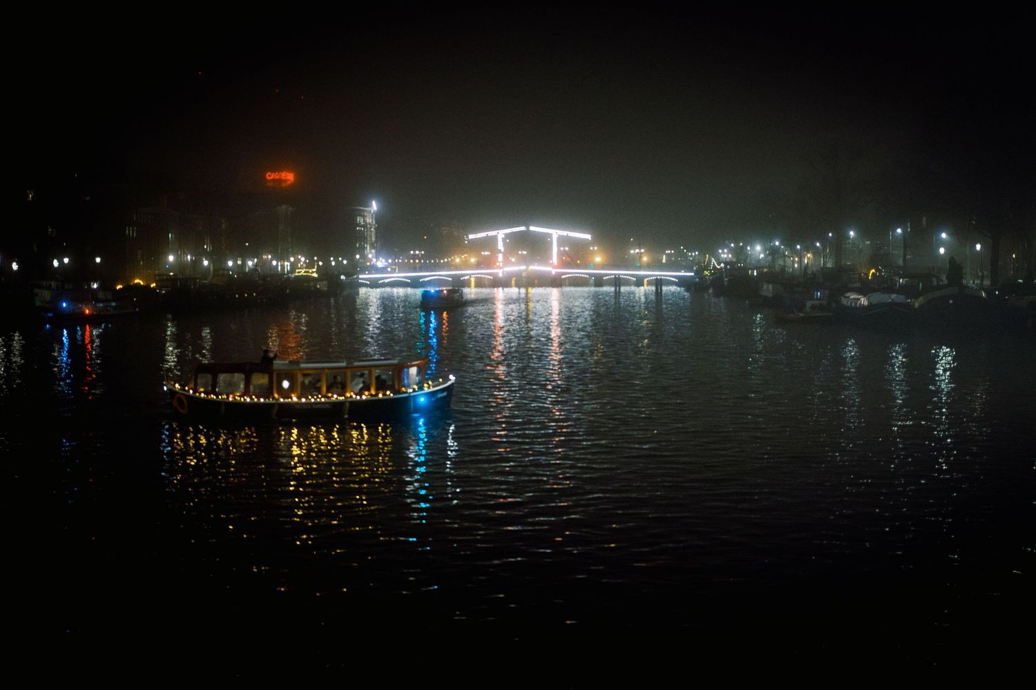 Night street photography in Amsterdam showing the city in heavy mist with soft lights, reflections and a cinematic urban atmosphere.