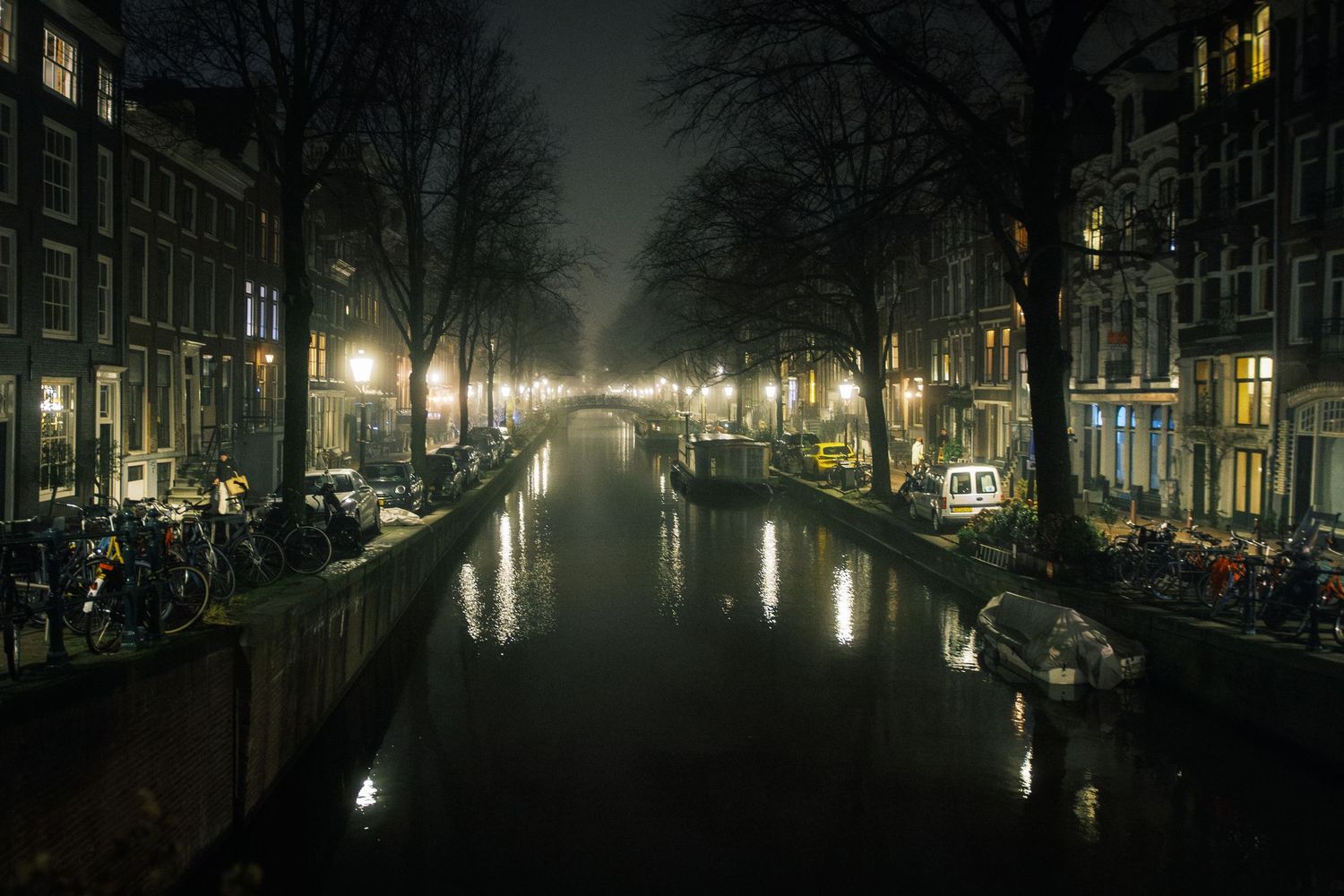 Night street photography in Amsterdam showing the city in heavy mist with soft lights, reflections and a cinematic urban atmosphere.