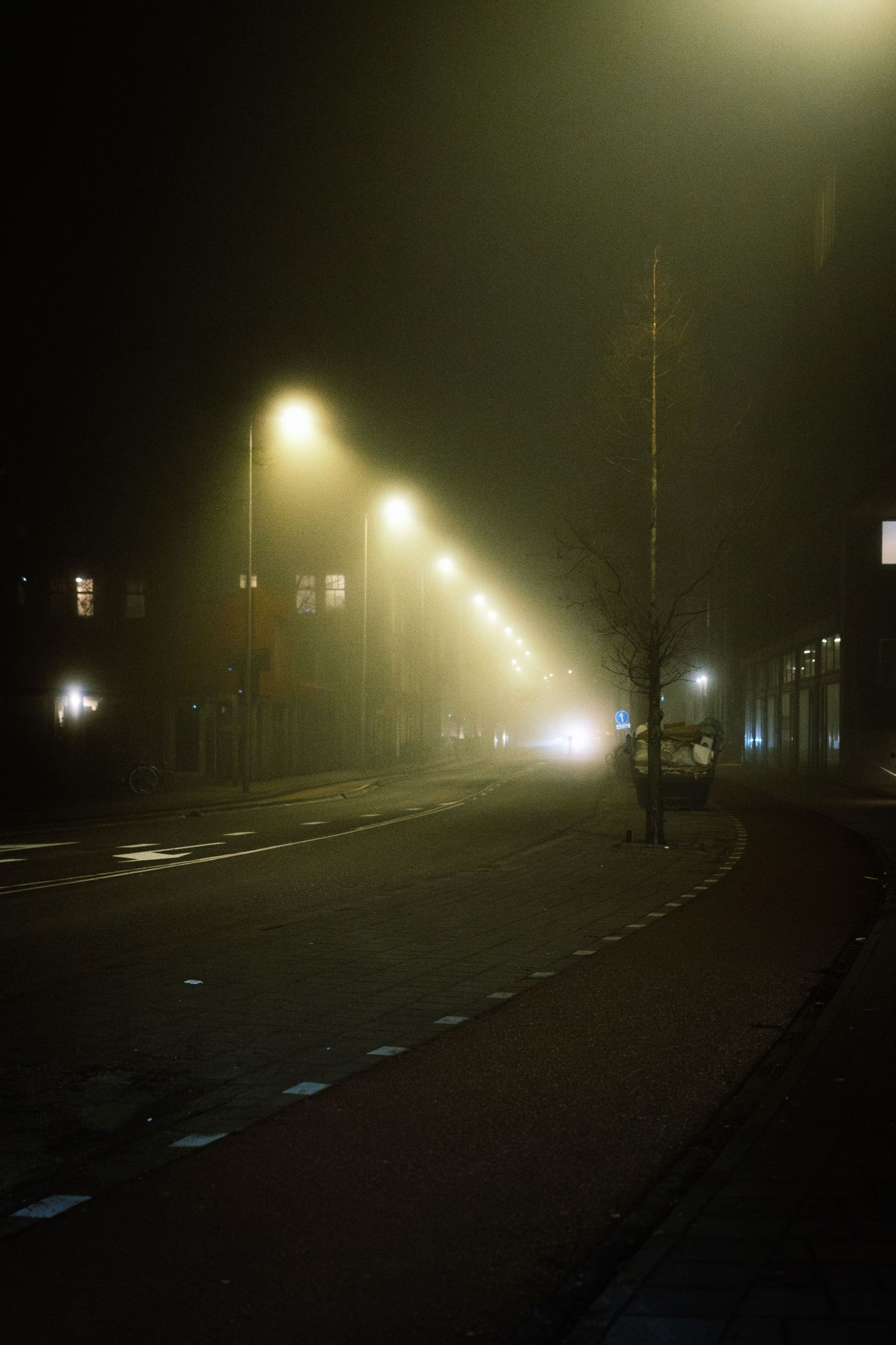 Night street photography in Amsterdam showing the city in heavy mist with soft lights, reflections and a cinematic urban atmosphere.