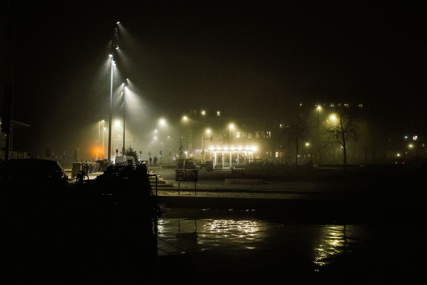 Night street photography in Amsterdam showing the city in heavy mist with soft lights, reflections and a cinematic urban atmosphere.