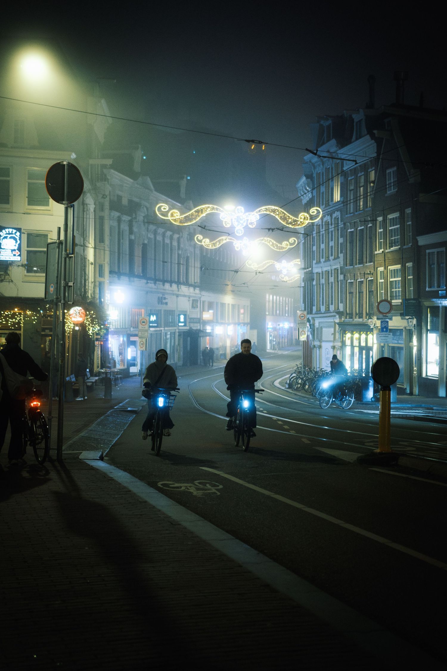 Night street photography in Amsterdam showing the city in heavy mist with soft lights, reflections and a cinematic urban atmosphere.