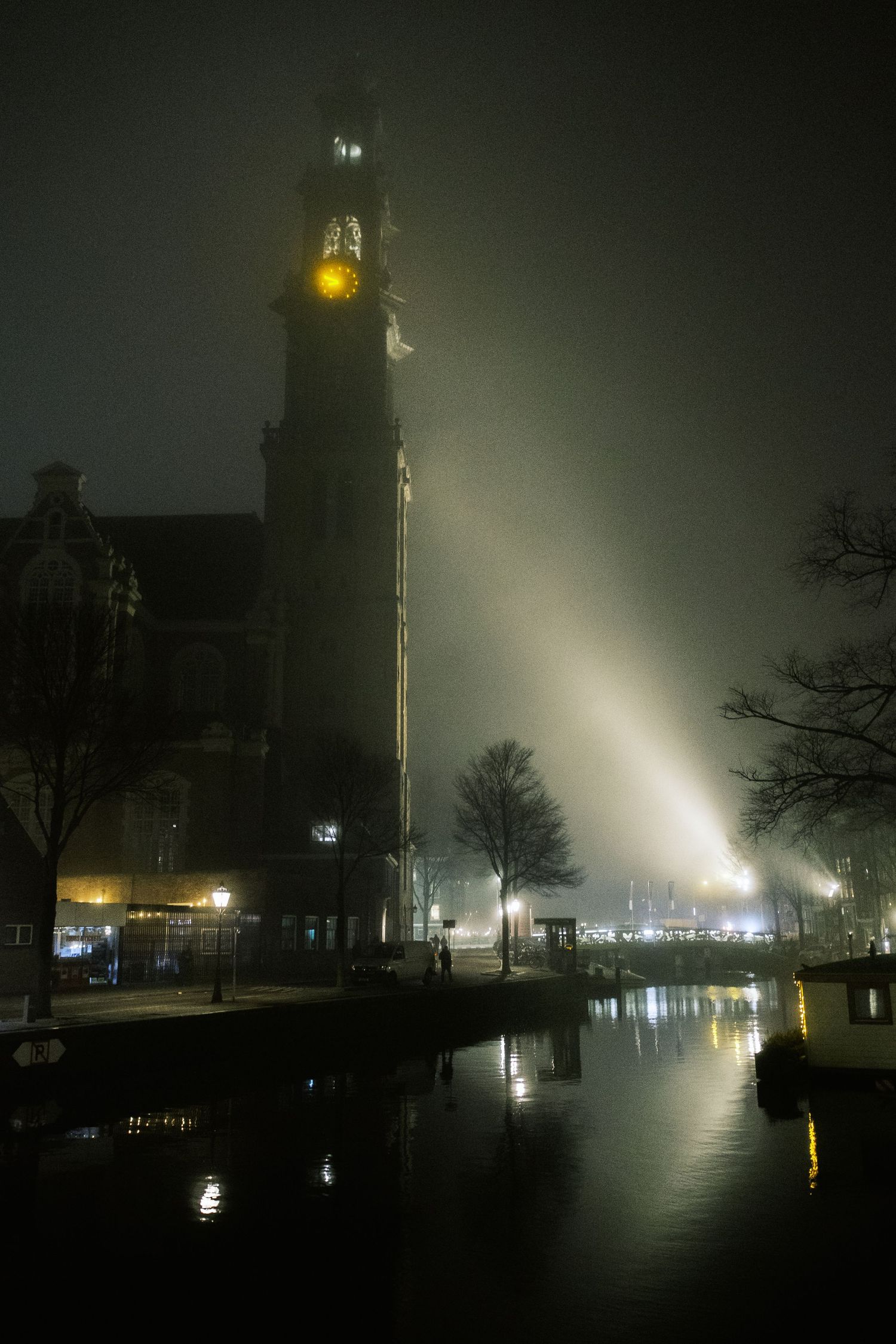 Night street photography in Amsterdam showing the city in heavy mist with soft lights, reflections and a cinematic urban atmosphere.