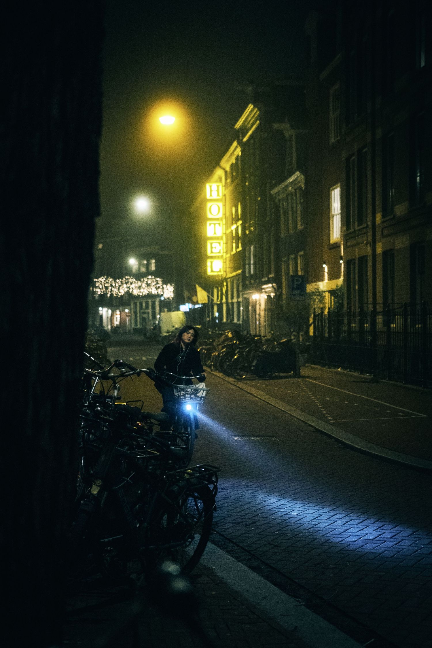 Night street photography in Amsterdam showing the city in heavy mist with soft lights, reflections and a cinematic urban atmosphere.