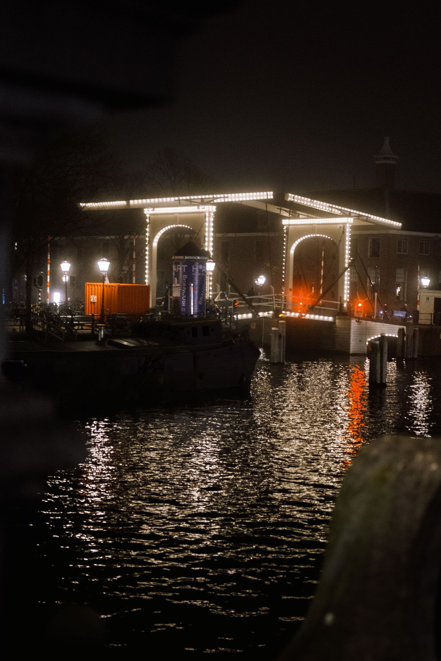 Night street photography in Amsterdam showing the city in heavy mist with soft lights, reflections and a cinematic urban atmosphere.