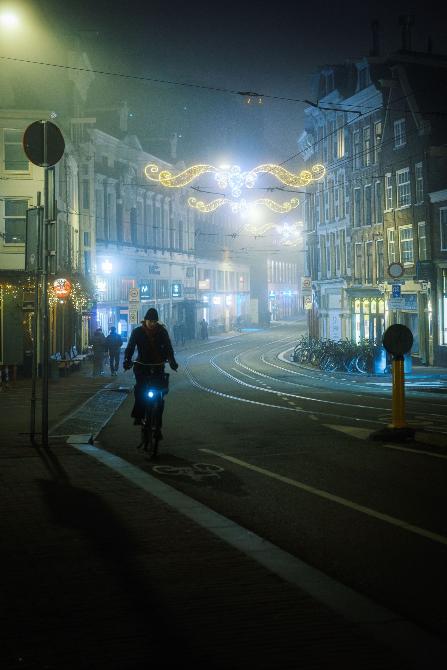 Night street photography in Amsterdam showing the city in heavy mist with soft lights, reflections and a cinematic urban atmosphere.