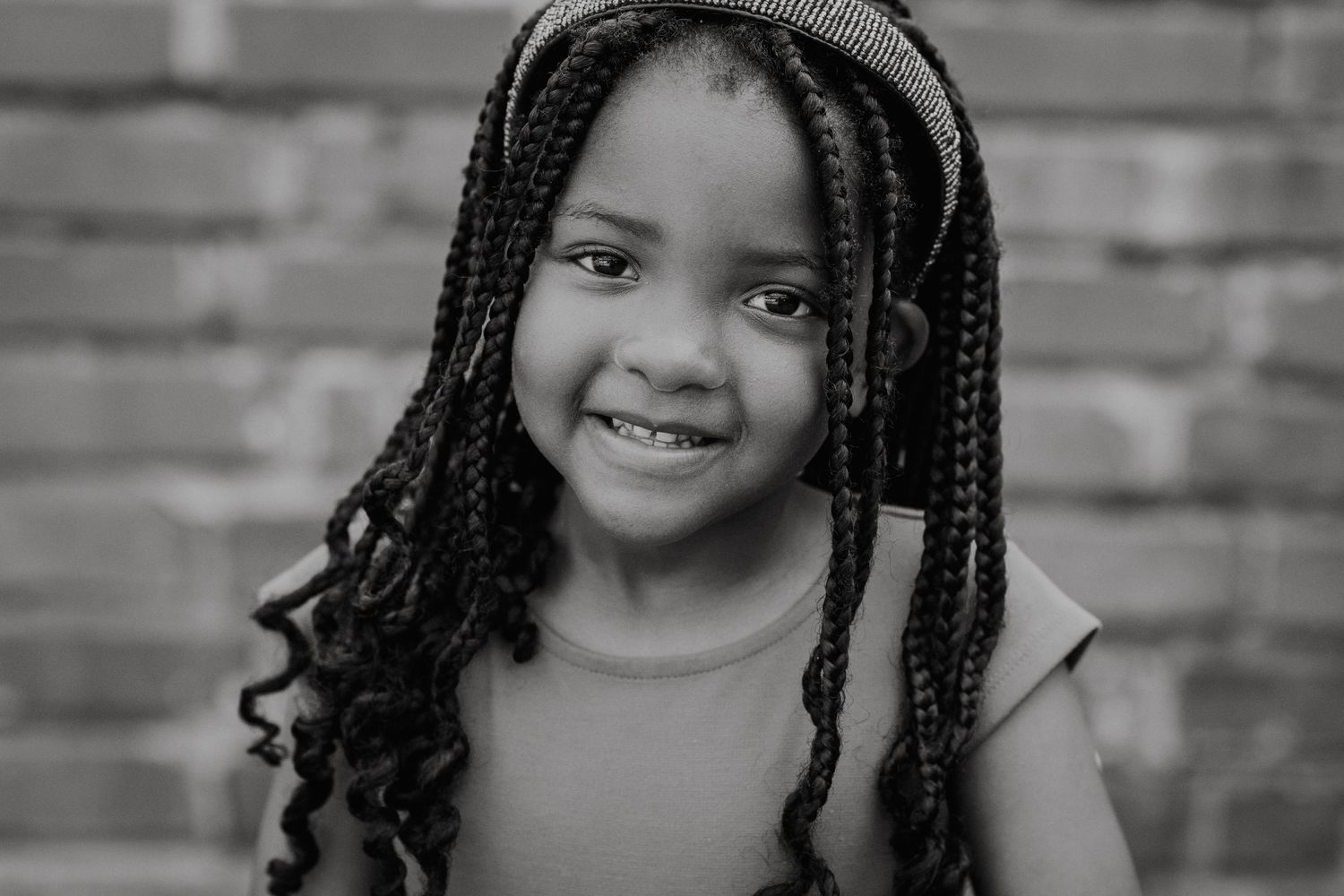 Candid portraits showing genuine smiles and braided hair against brick wall.