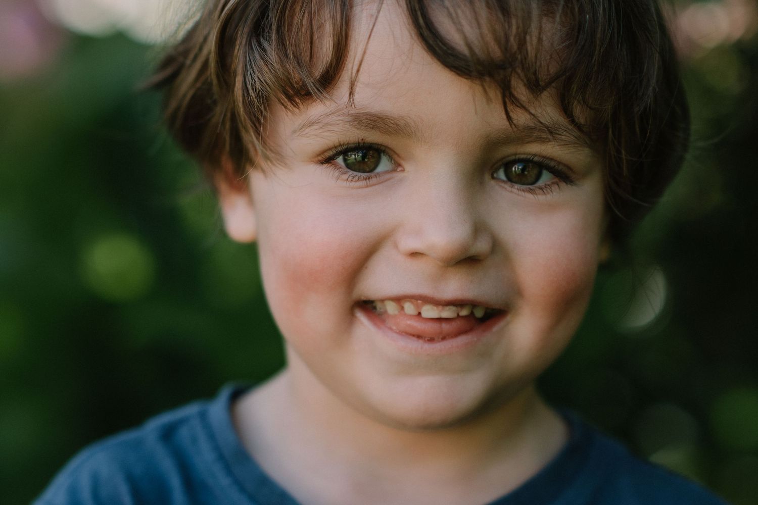 Close up portrait showing a bright smile and sparkling eyes against natural greenery.