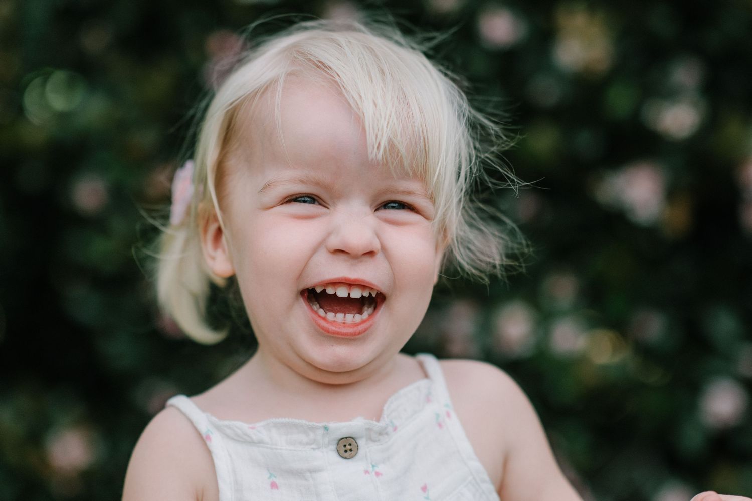 Portrait of a joyful young child laughing outdoors against a blurred floral background.