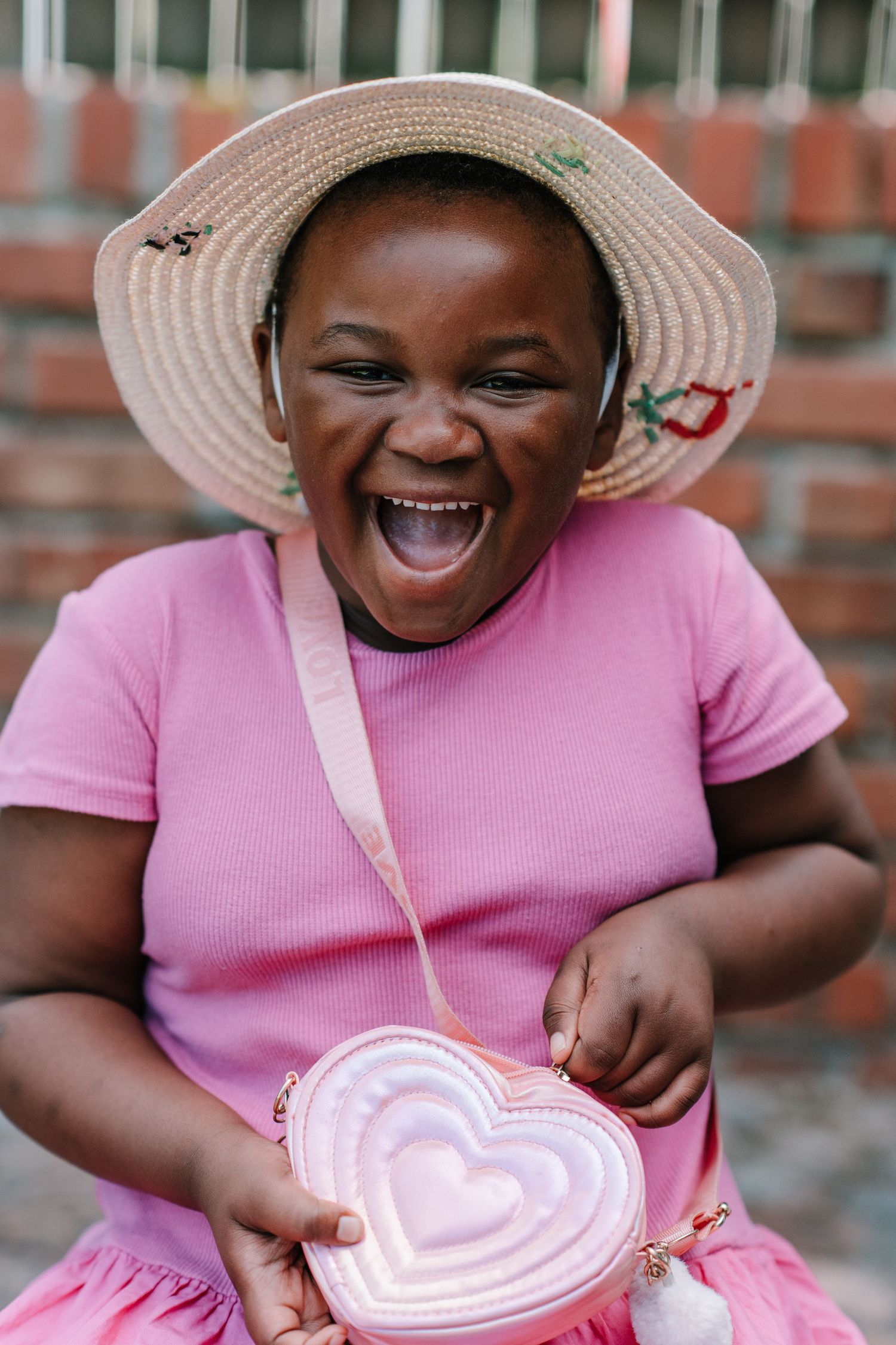 A joyful moment captured in pink showing pure delight while holding a heart-shaped item against a brick wall background.