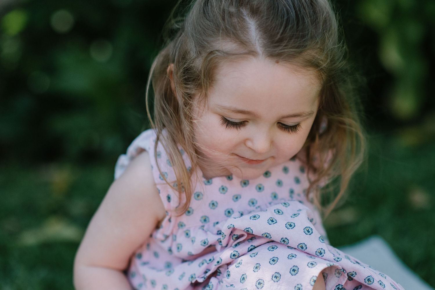 Child wearing a floral print dress playing outdoors in a garden setting.