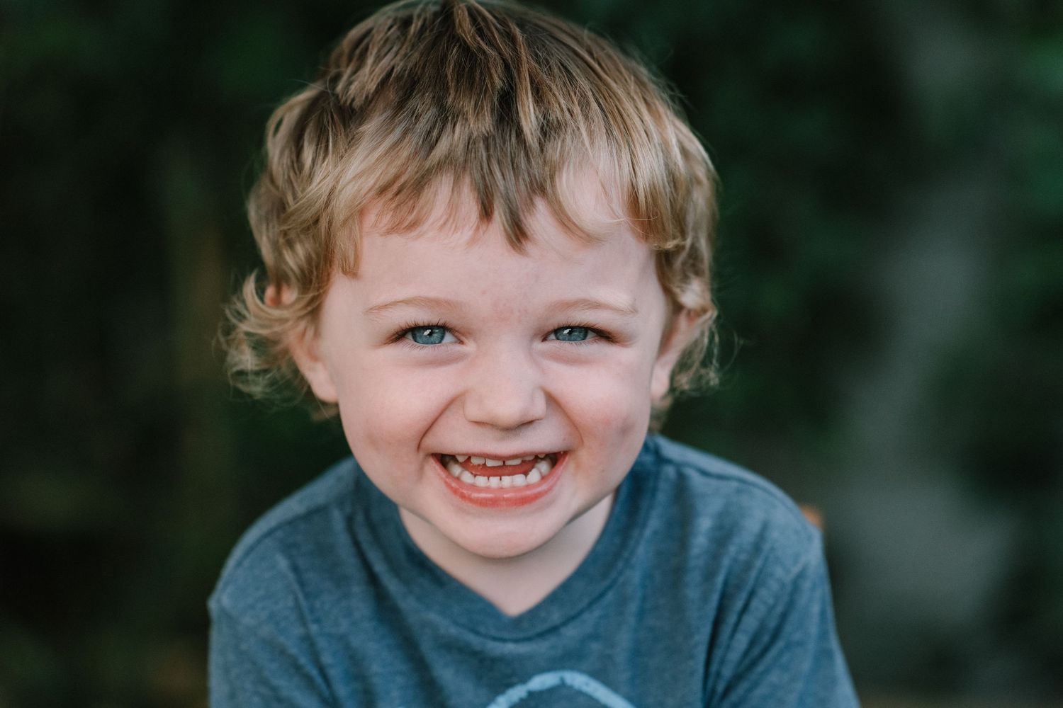 Child in blue shirt smiles warmly against dark background.