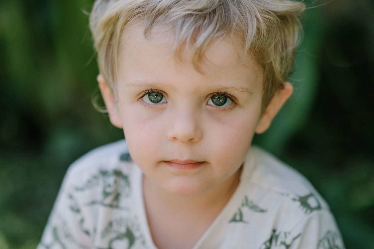 Close-up portrait of a young child with bright eyes against a natural green background.