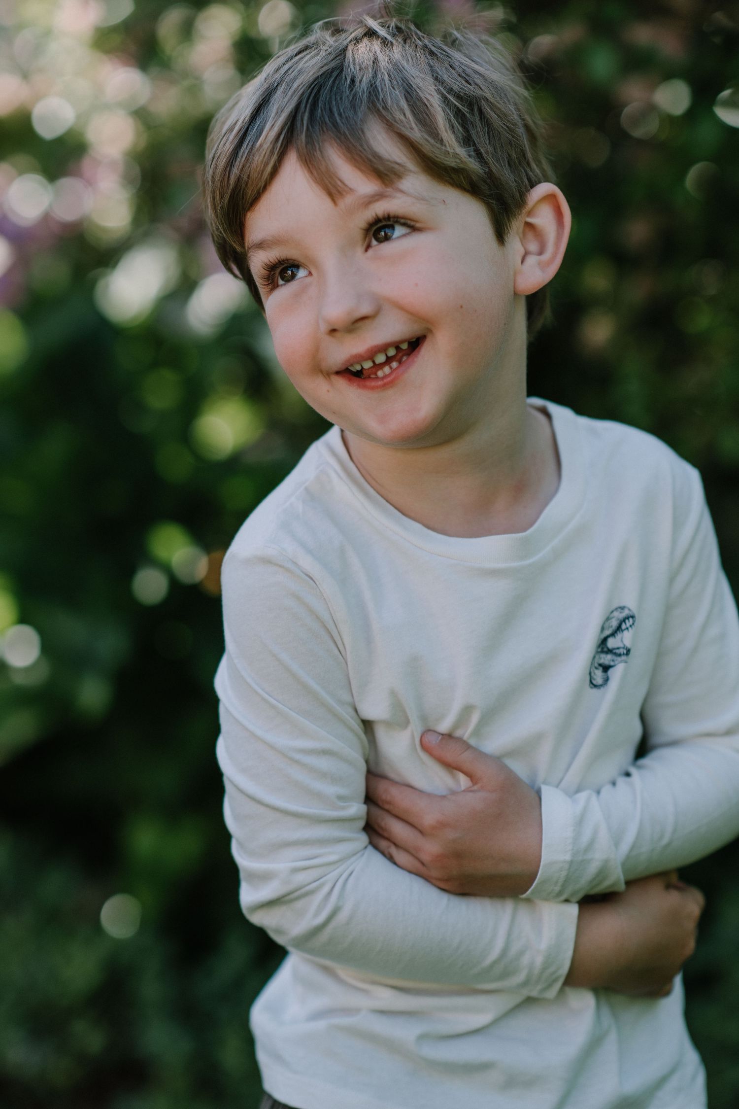Candid shot of a child in a white sweater laughing and hugging themselves outdoors.
