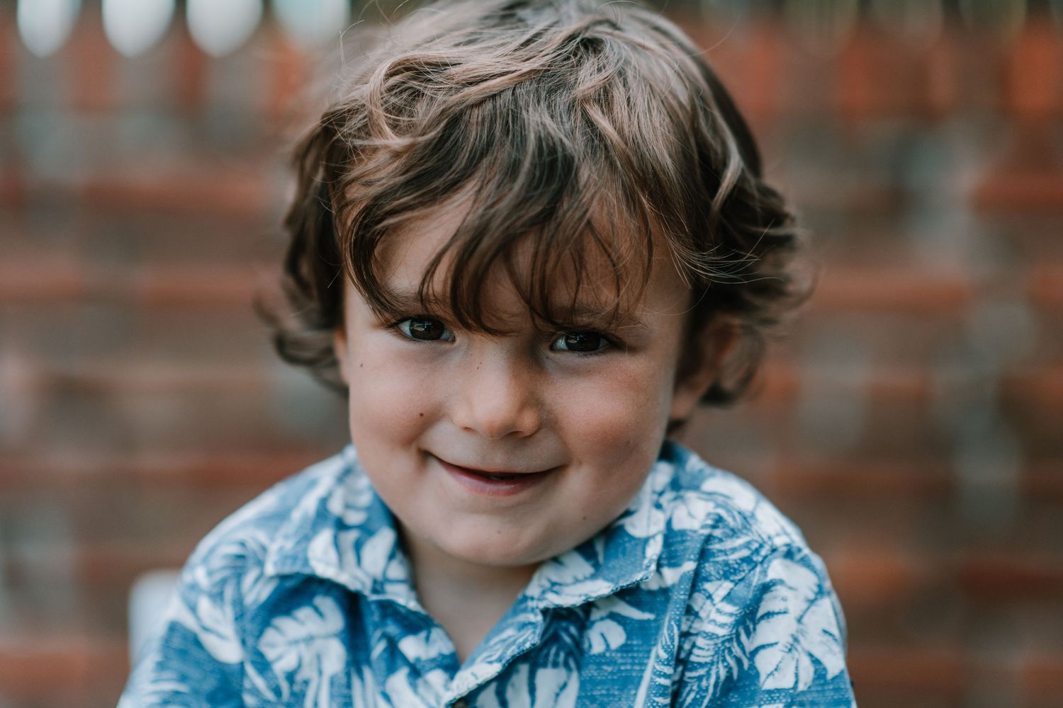 Close-up portraits in a blue floral shirt against rustic brick background.