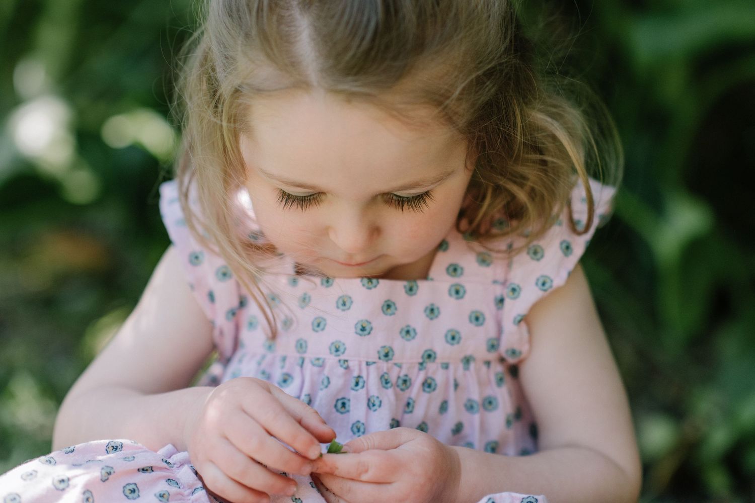 Child in floral dress playing shyly in an outdoor garden setting.