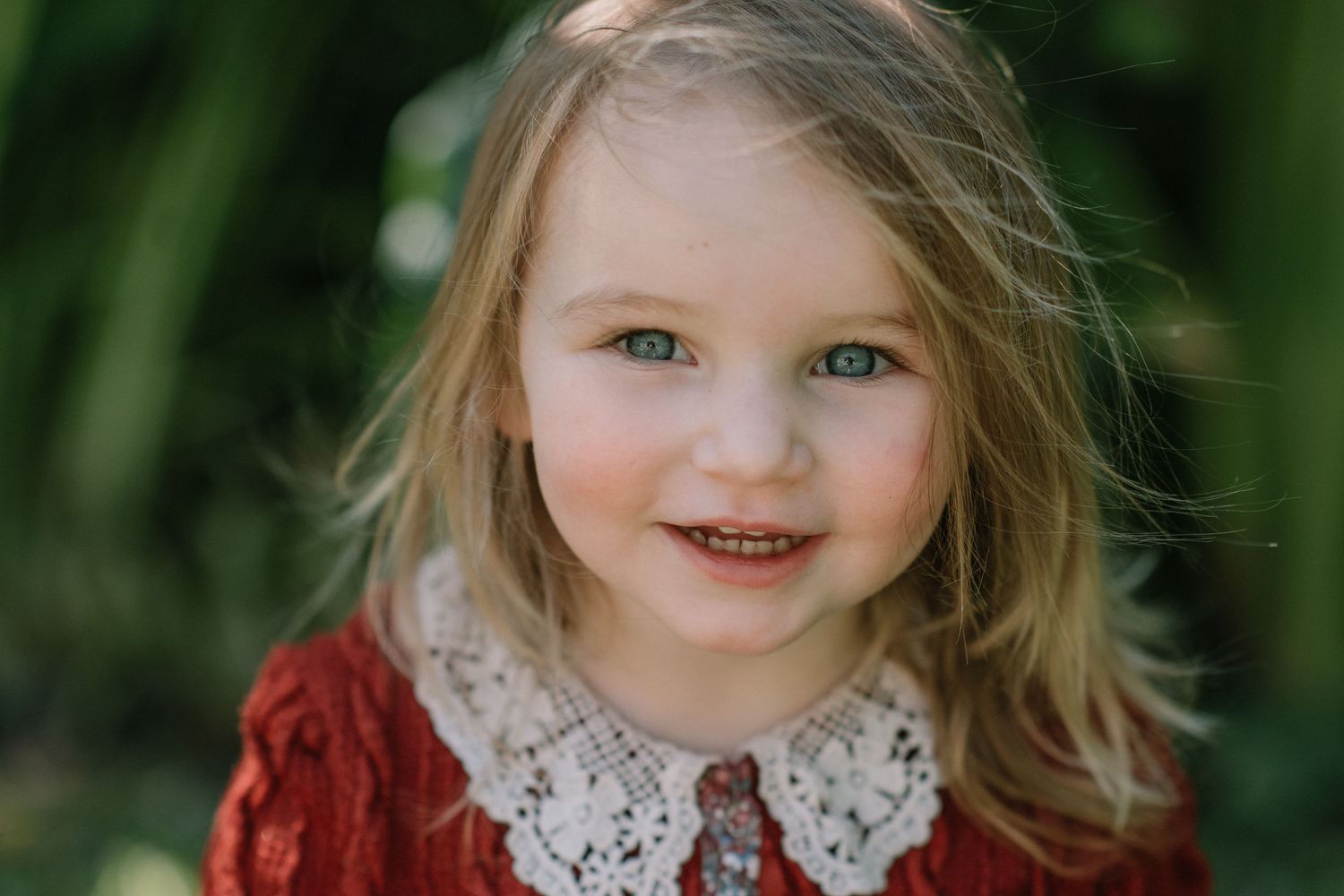 Joyful outdoor portrait with natural lighting and lush greenery.