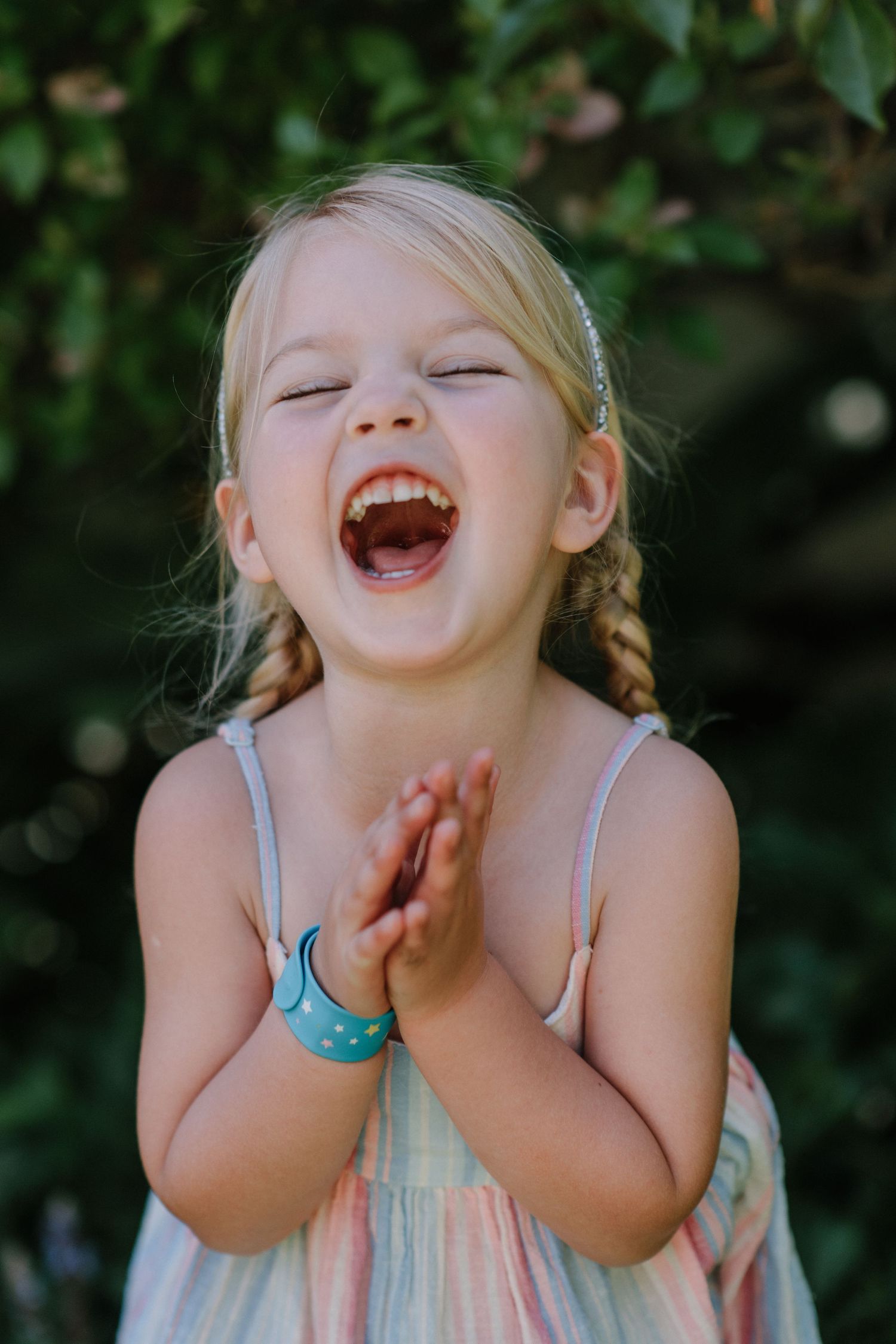 Joyful child with braids laughing with closed eyes while clapping hands in a summer dress.