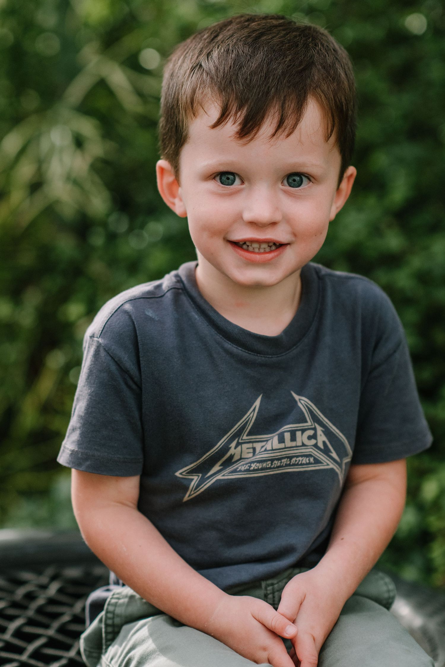 Child wearing Metallica band t-shirt poses outdoors with a happy smile.