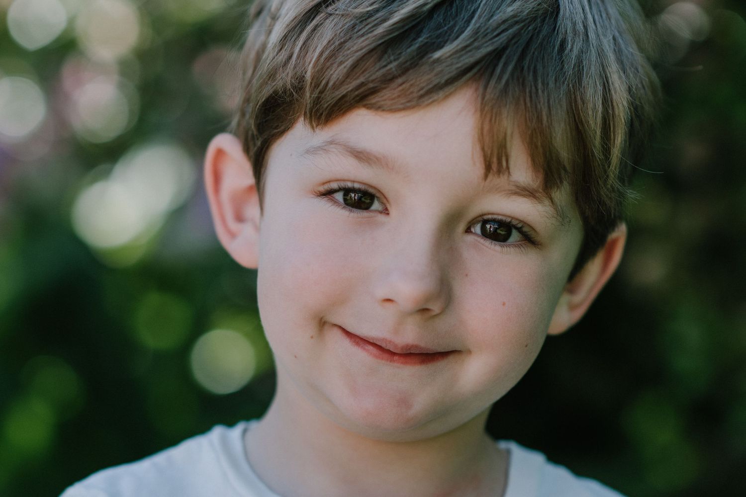 Close up portrait of a young child smiling softly against a blurred green outdoor background.