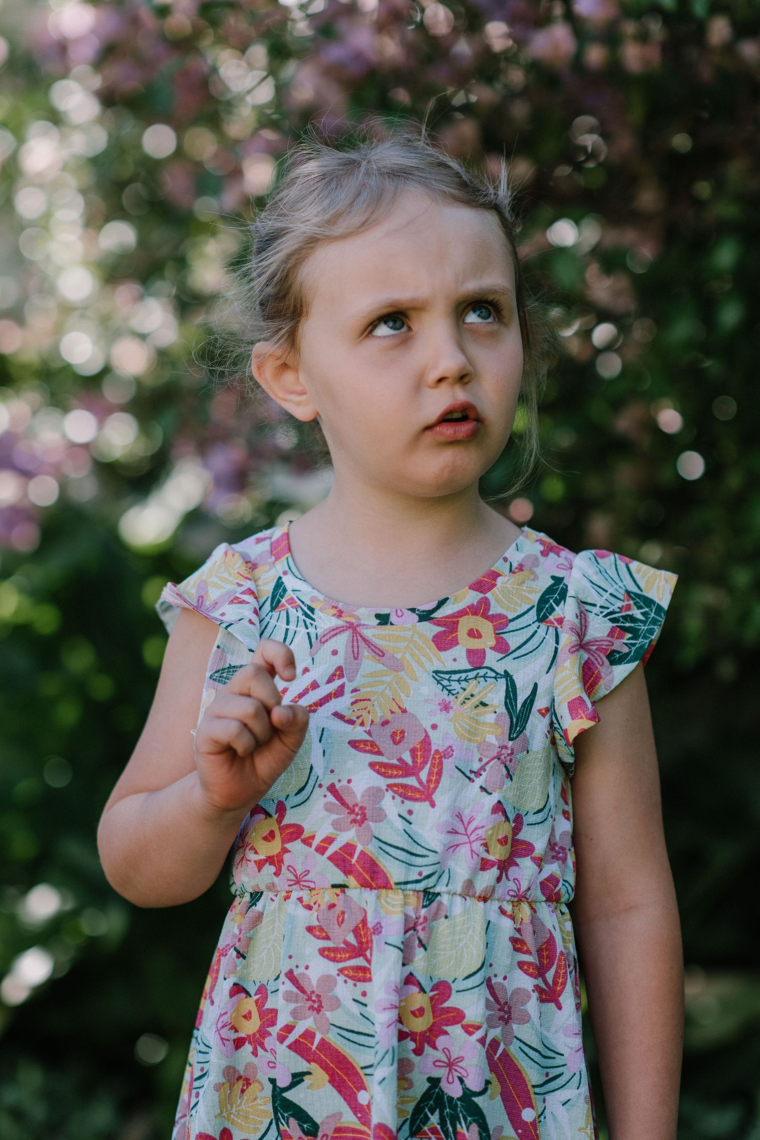Child wearing summer floral dress poses expressively in garden setting.