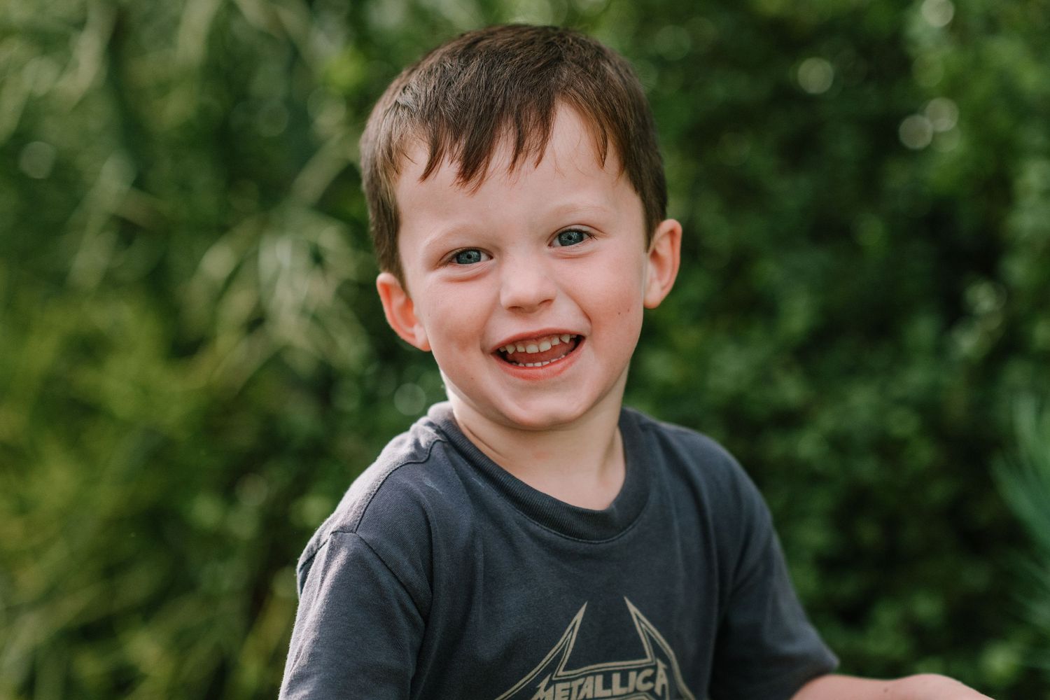 Young child in black t-shirt sits outdoors with joyful expression.