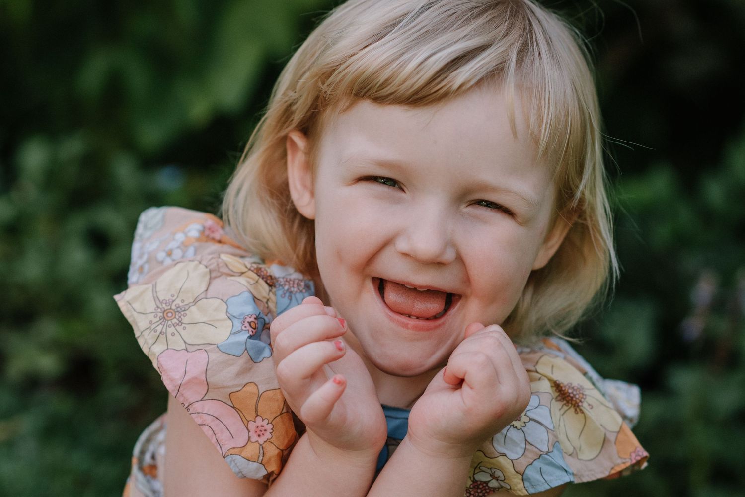 Child with rosy cheeks giggling while wearing floral print sleeves outdoors.