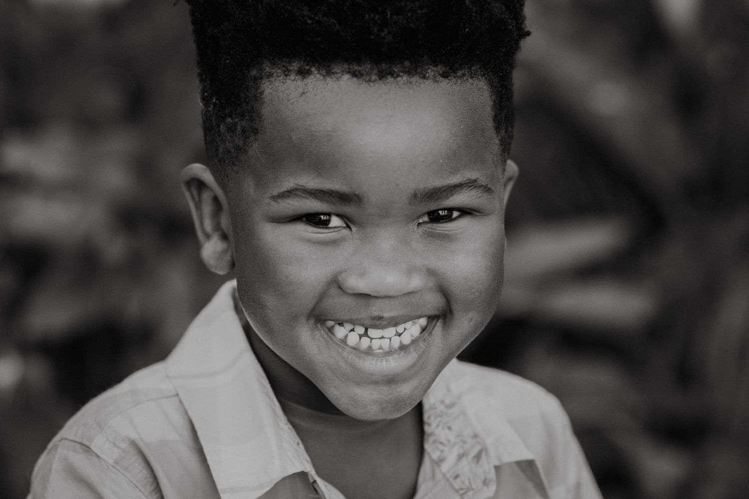 Black and white portrait of child showing bright smile against dark background.