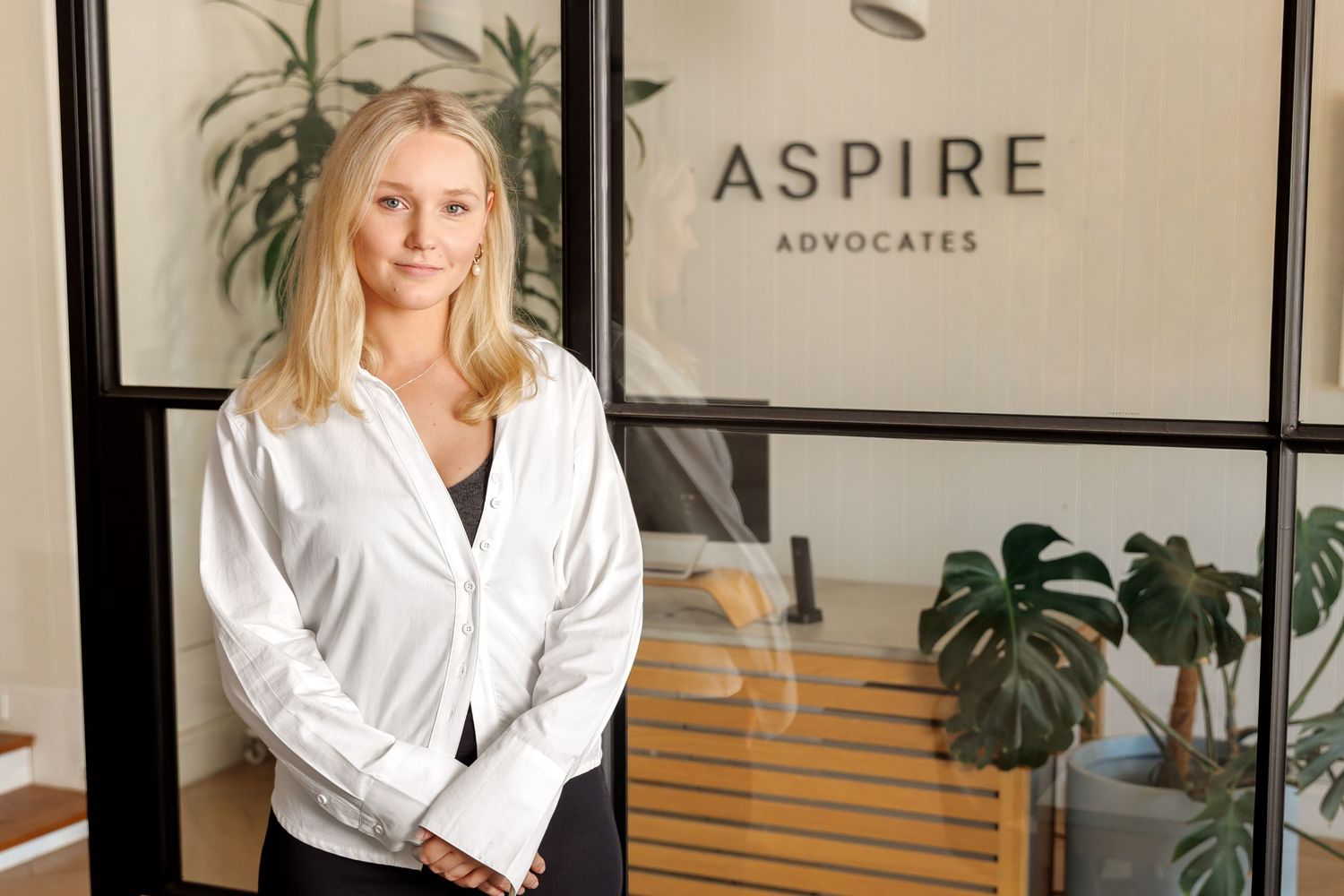 Professional business portrait of a woman in a modern office interior with plants, soft natural light and neutral tones.