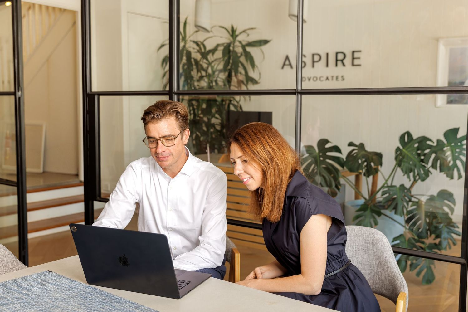 Business professionals collaborating on a laptop in a modern office with indoor plants, natural light and minimalist interior.